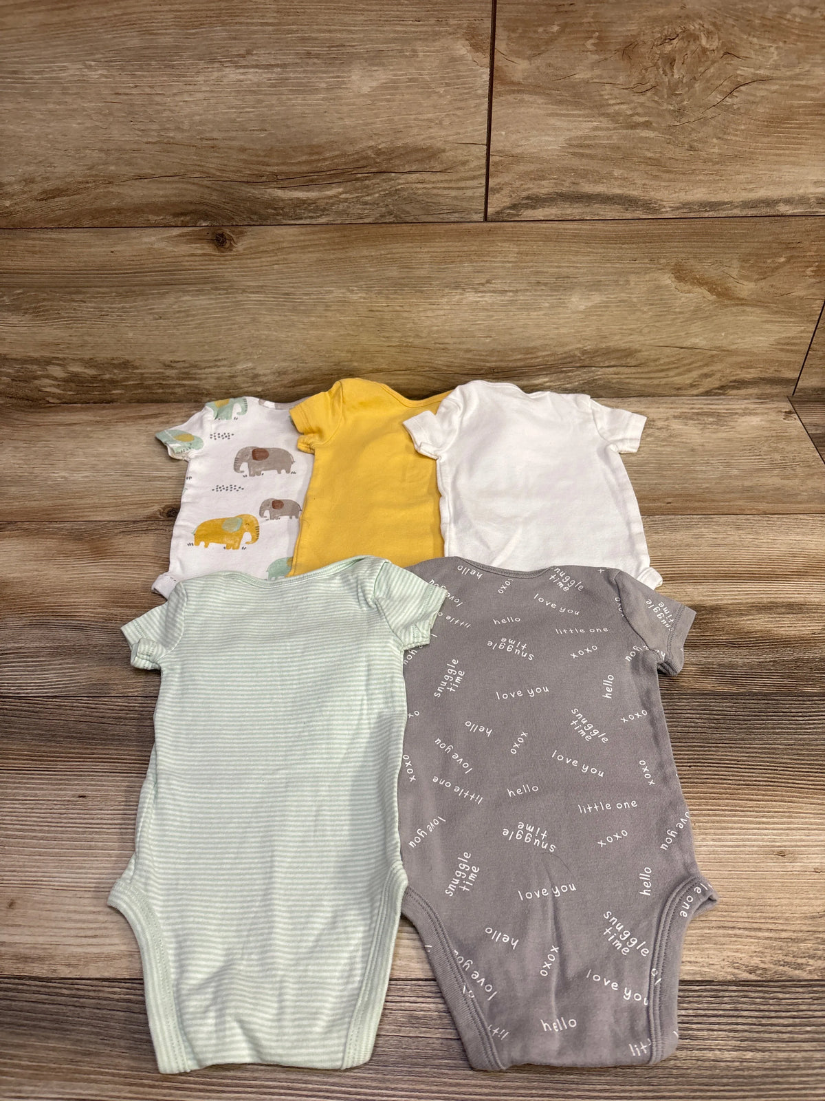 Top down view of Carters five pack baby bodysuits in white yellow gray green stripes and animal print on a wood floor
