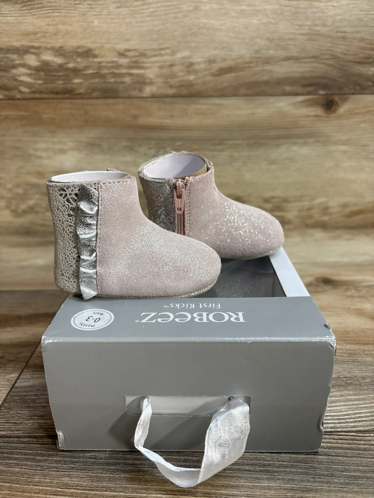pink glittery baby boots with zipper and silver ruffle on branded gray shoe box on wood floor