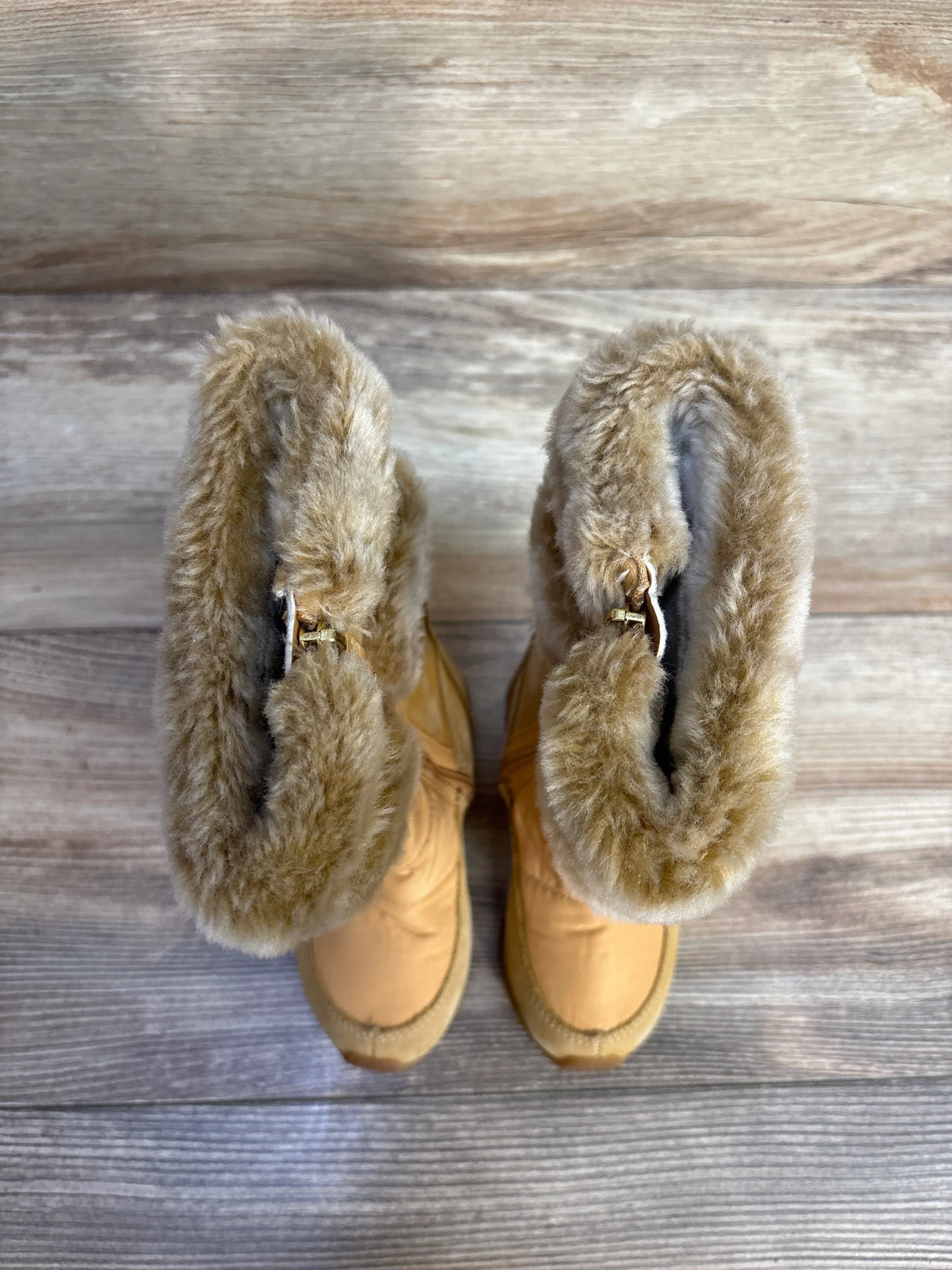 Tan faux fur lined winter boots on wooden floor, top view
