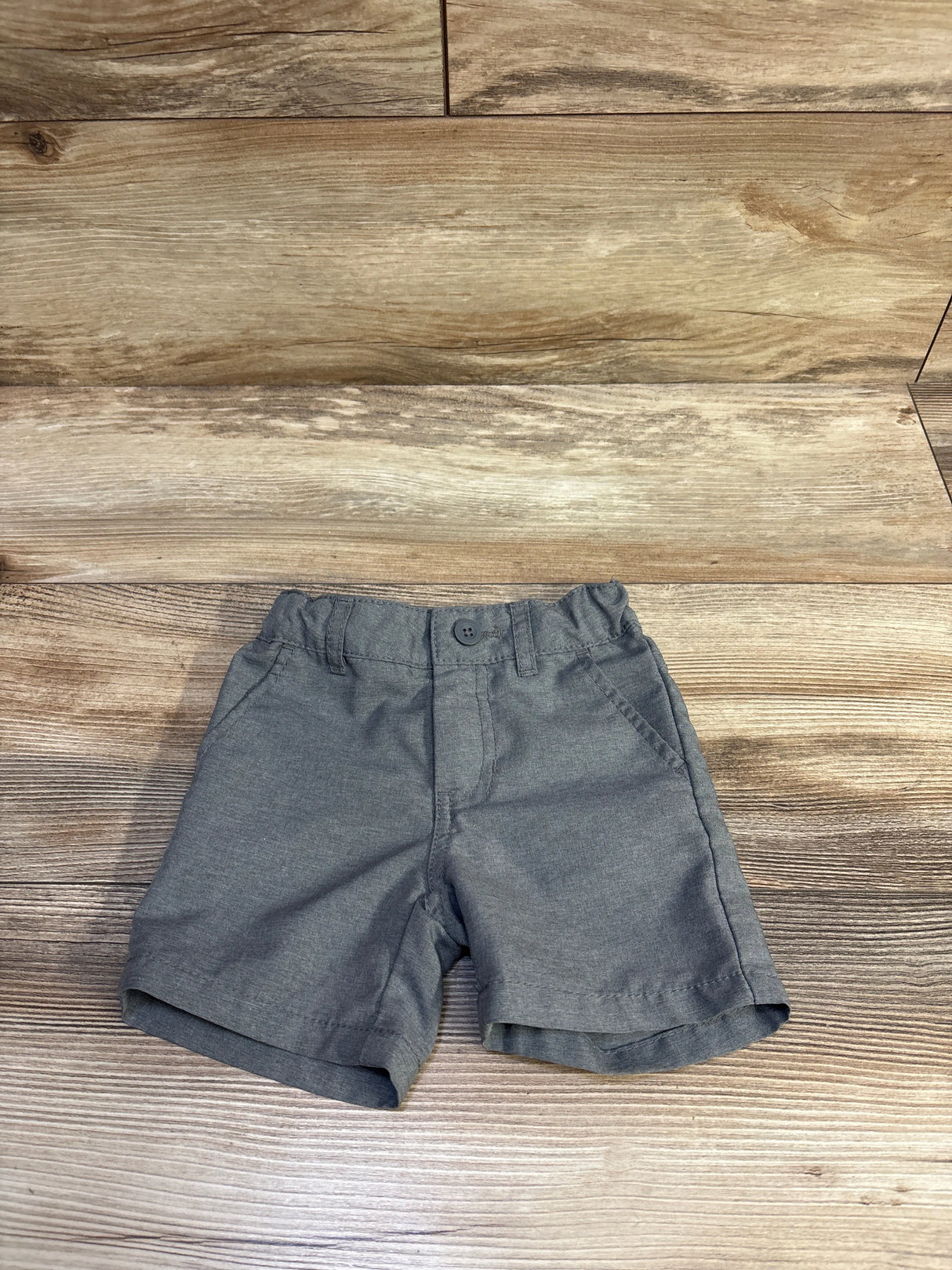 Top view of grey toddler chino shorts showing elasticized waist, front button, and side pockets on wood background