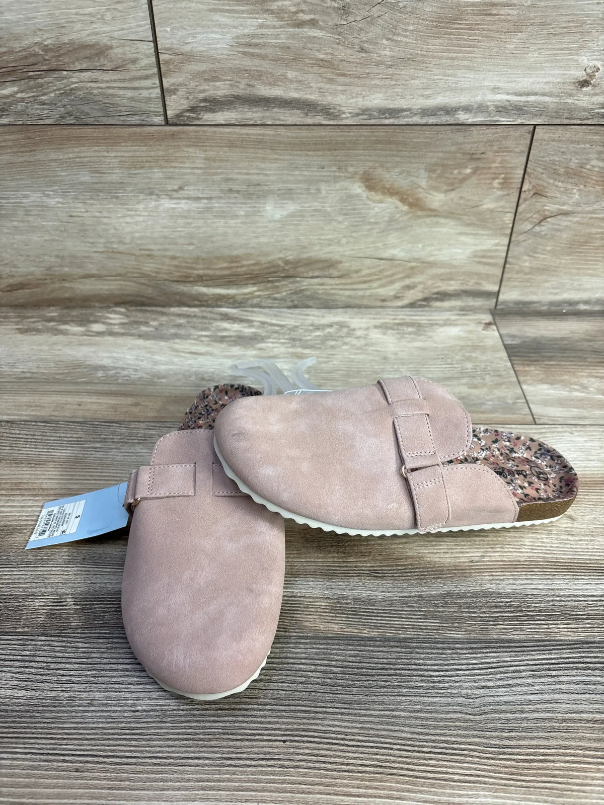Pink suede slip-on clogs with floral printed insole and adjustable strap on wooden floor background