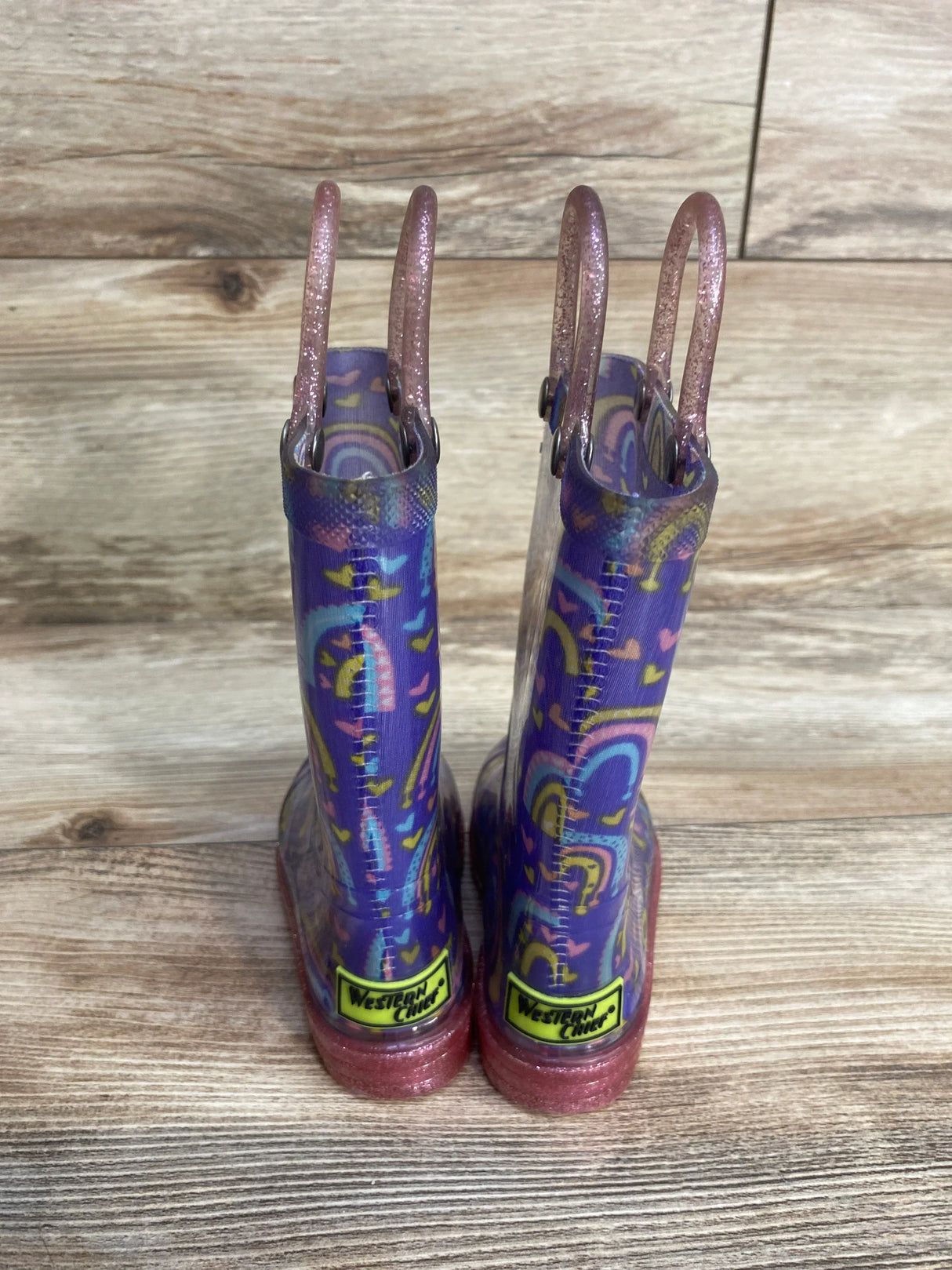 Kids' purple Western Chief rain boots with glitter handles and colorful swirl pattern on wood floor