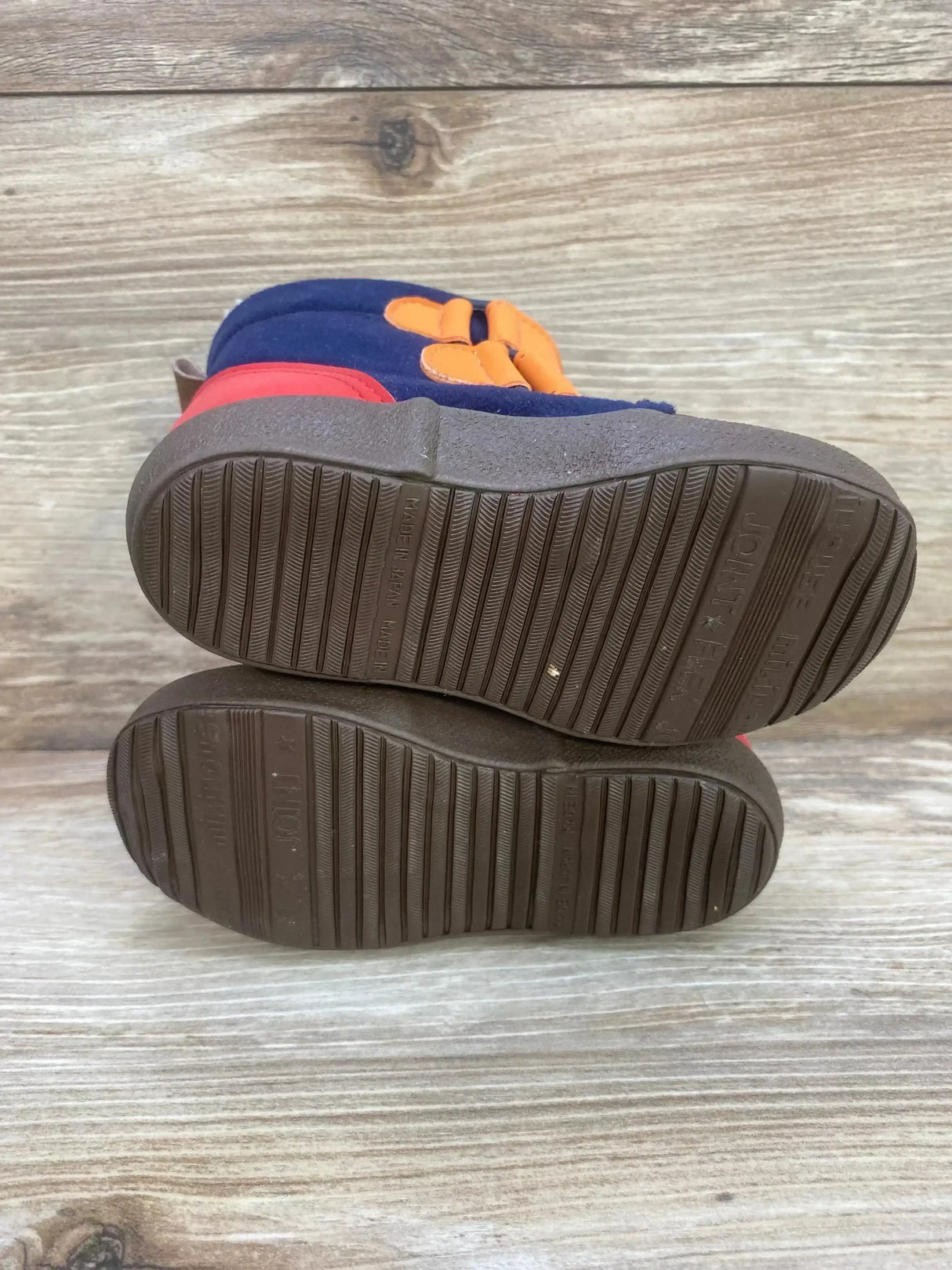 Bottom view of Double B miki House boots size 6 showing brown grooved soles, navy with orange straps on wood background