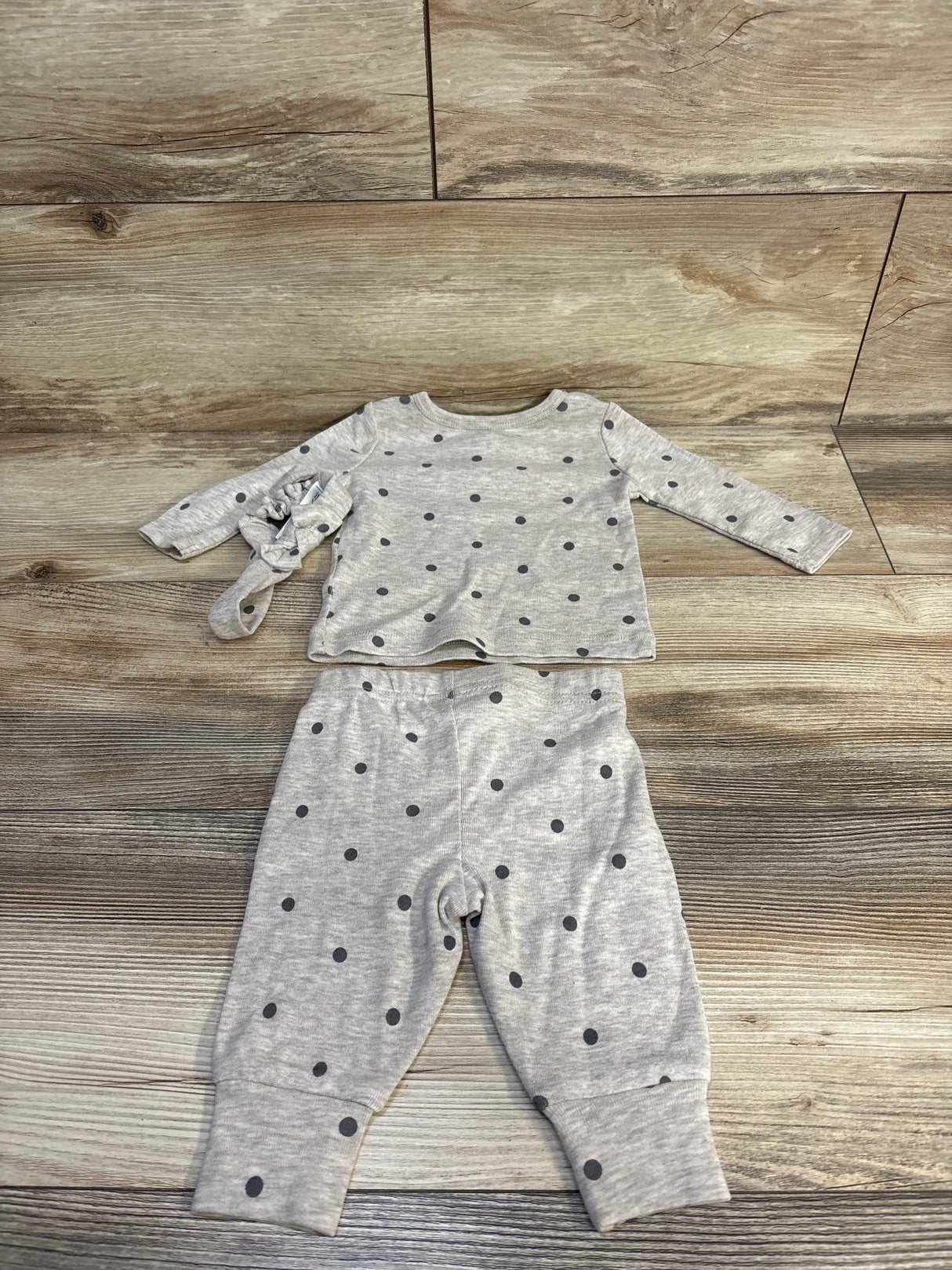 Flat lay of tan 3-piece polka-dot baby set showcasing long-sleeve shirt, pants, and matching headband on wood floor