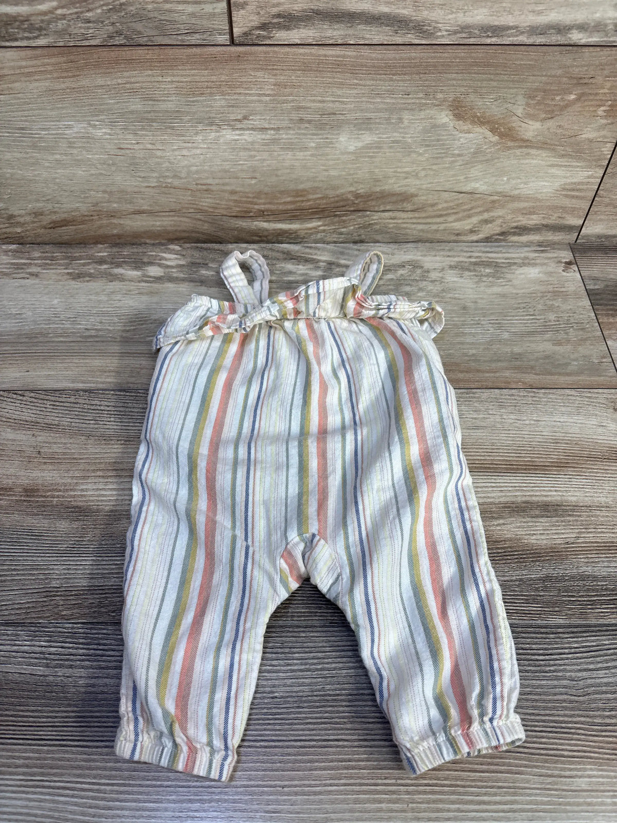 Front view of Carter’s ivory striped jumpsuit showcasing multicolor stripes and elastic ankle cuffs on a wood-grain surface
