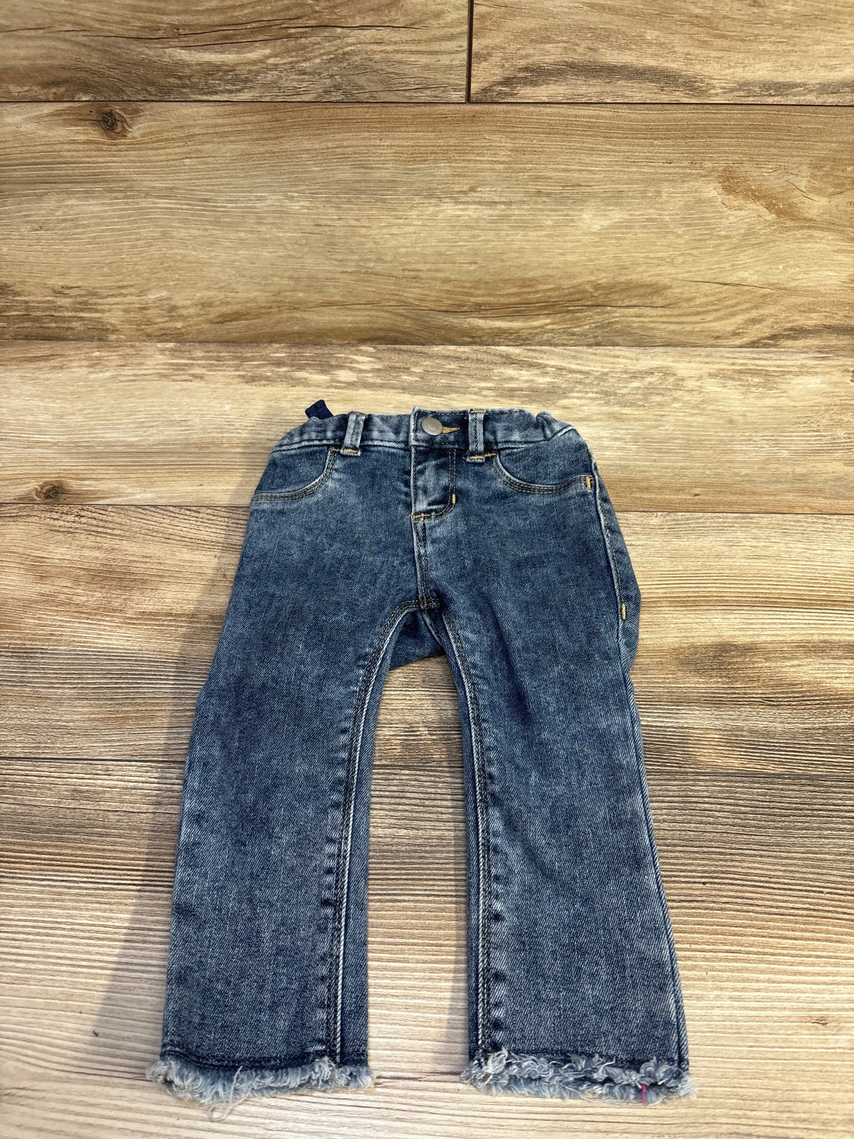 Front view of blue toddler jegging jeans size 18-24M showing elastic waistband, faux pockets and frayed hems on wood