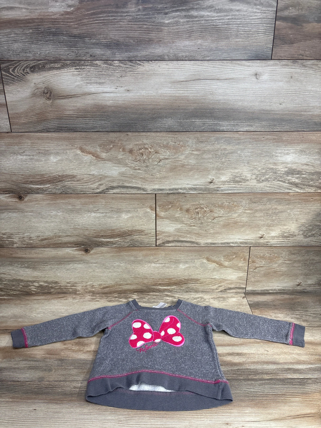 Front view of grey Disney Minnie Mouse toddler sweatshirt (4T) showing pink polka-dot bow applique and pink topstitching on wood floor background