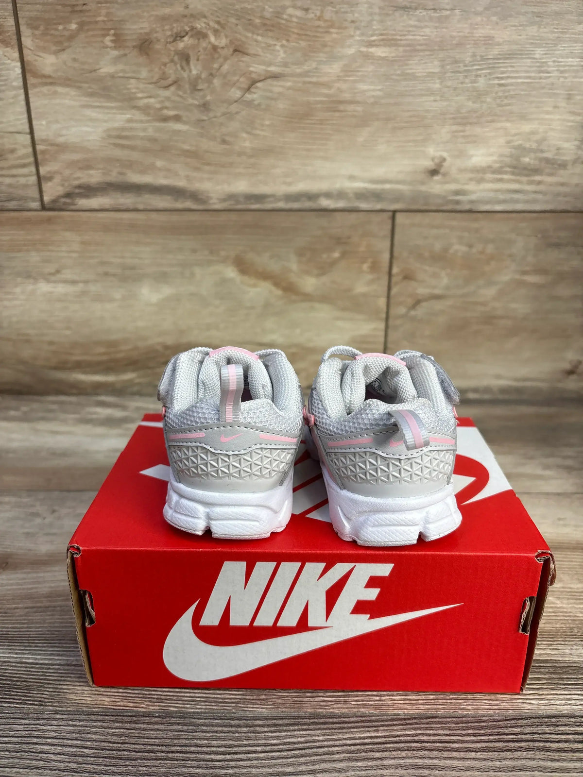 Rear view of toddler Nike Vomero 5 TD sneakers in grey, soft white and pink showing textured heel and pull tabs on red Nike box