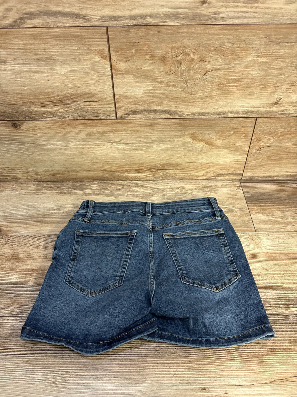 Rear view of Gap maternity shorts with 4-inch inset panel, dark wash denim, and two functional back pockets on a wood floor
