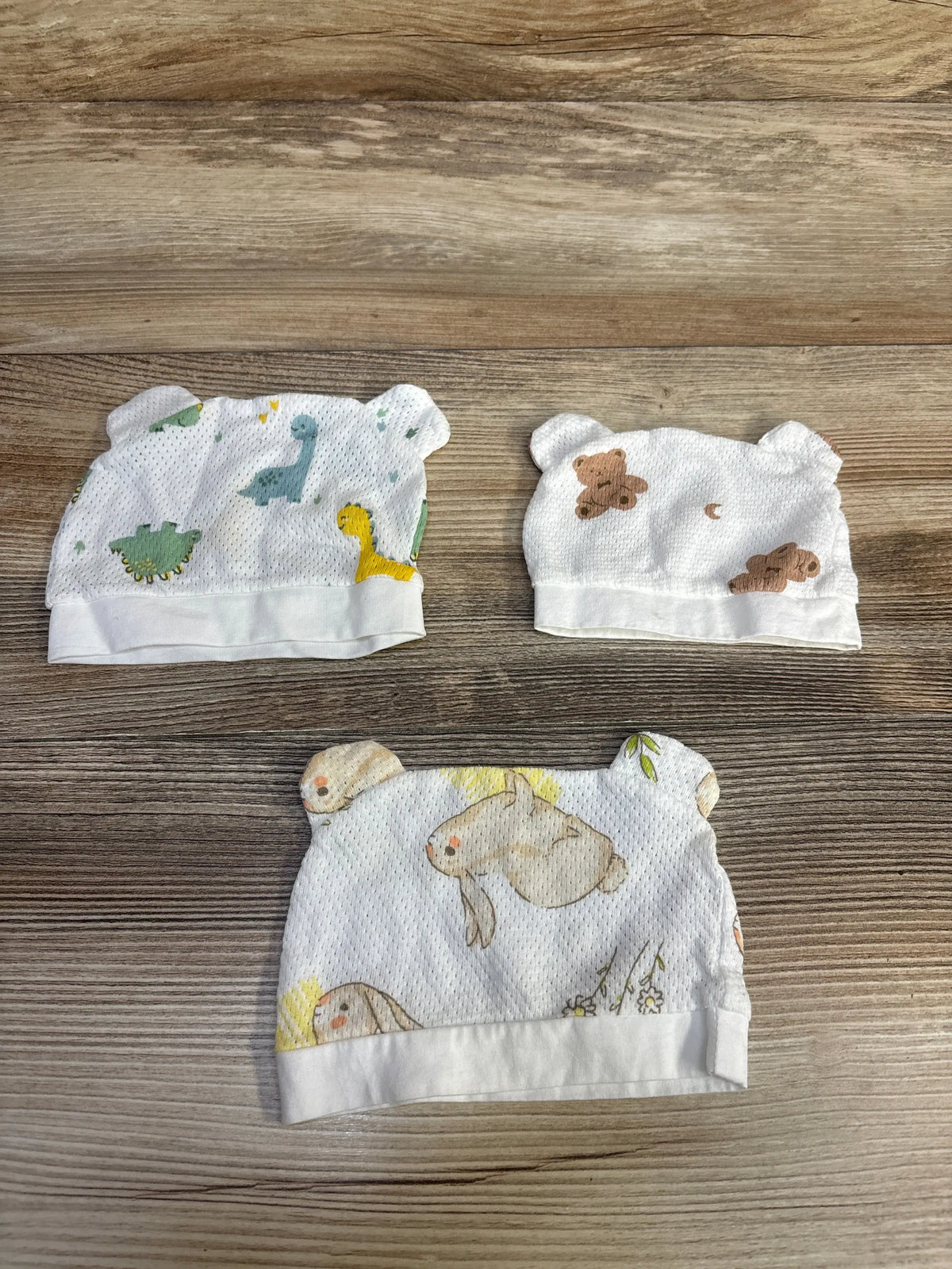 Top view of three Mesh Animal Print Newborn Hats with Ears showcasing mesh fabric and animal prints on a wood surface