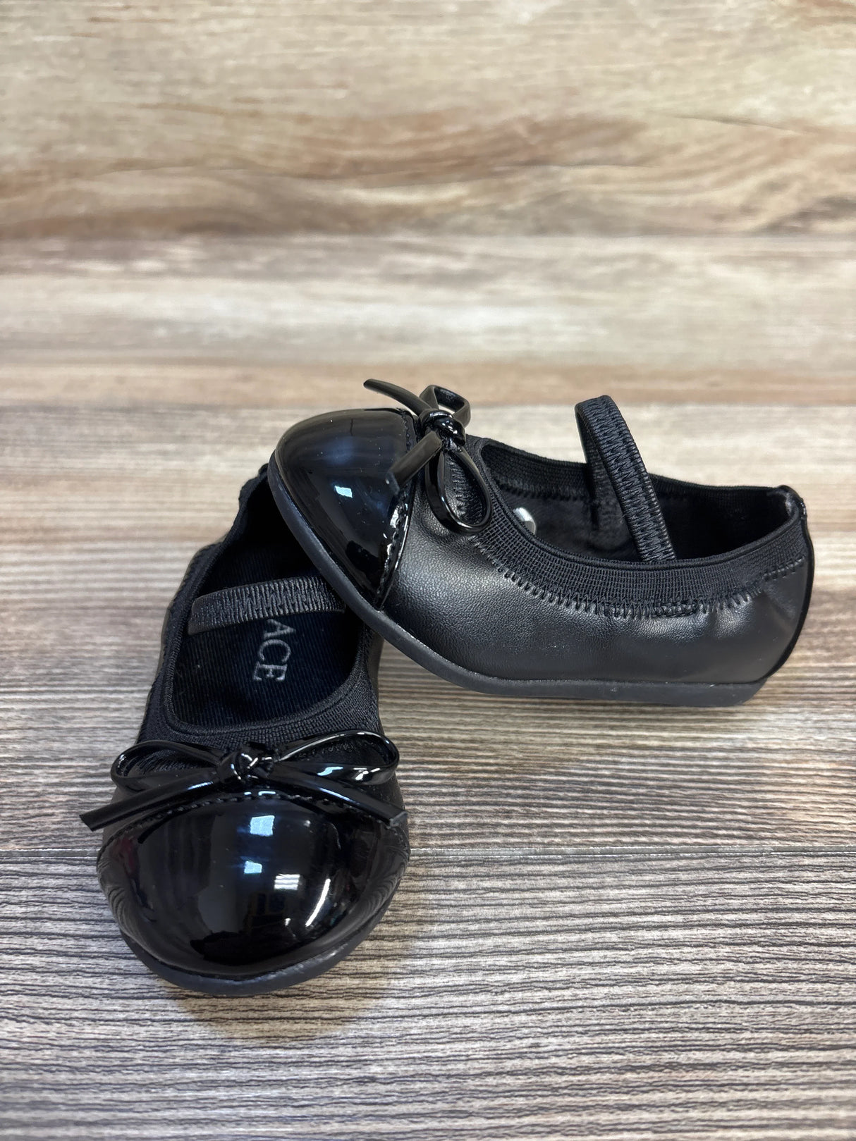 Black toddler dress shoes with bow detail on wooden surface