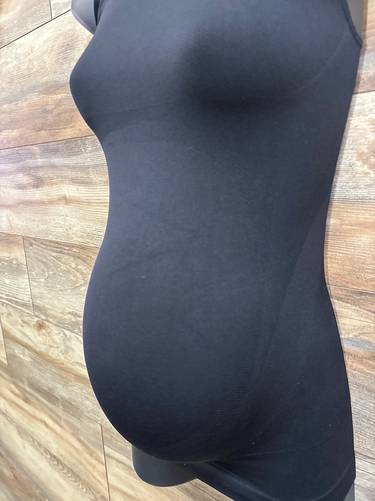 Side view of black Blanqi maternity SportSupport crossback tank top on mannequin showing built-in tummy support against wood plank background