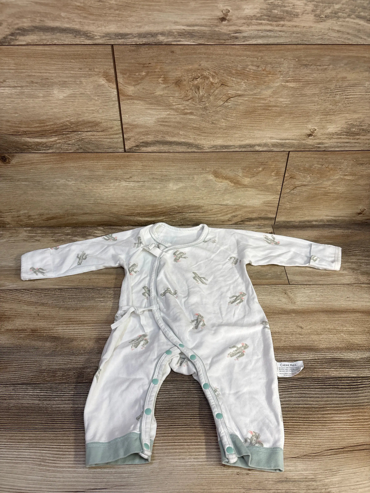 Front view of Cherie Kids white cactus print footless kimono sleeper showcasing wrap front and snap closures on a wood floor
