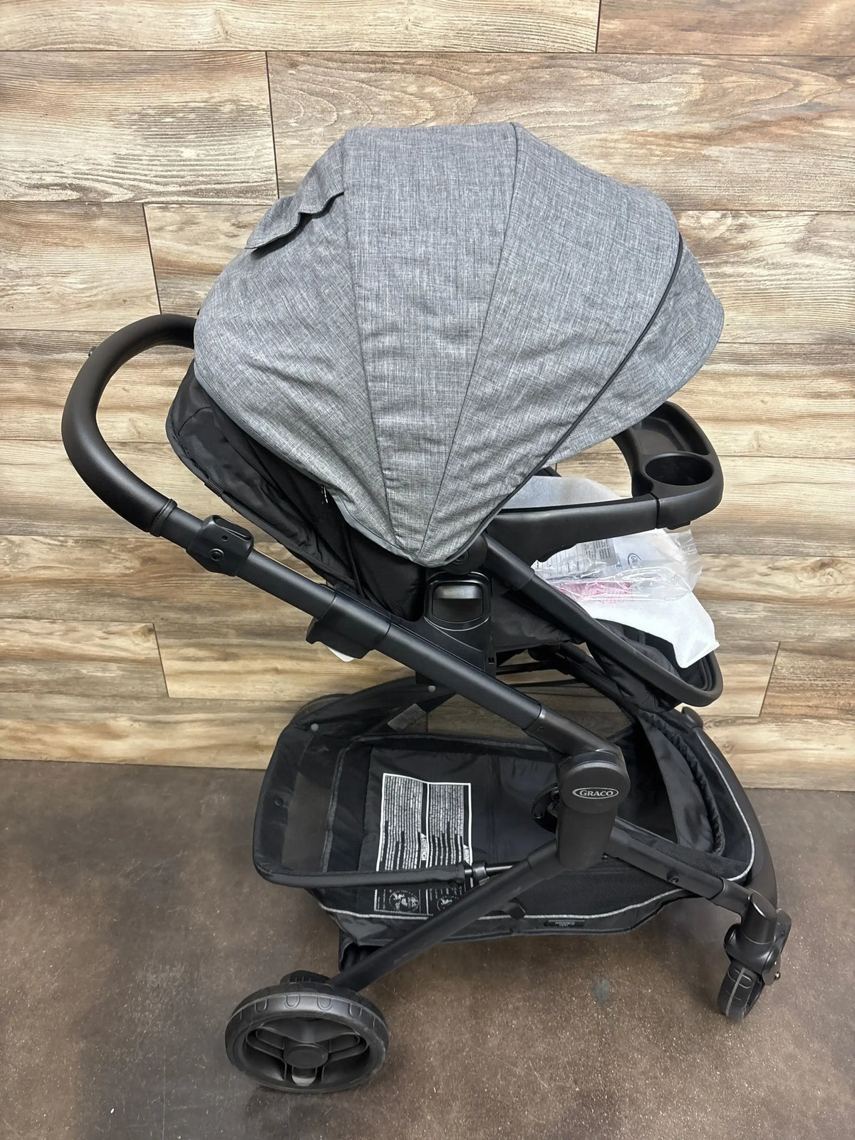 Gray Graco baby stroller with canopy, cup holders, and storage basket on wood floor