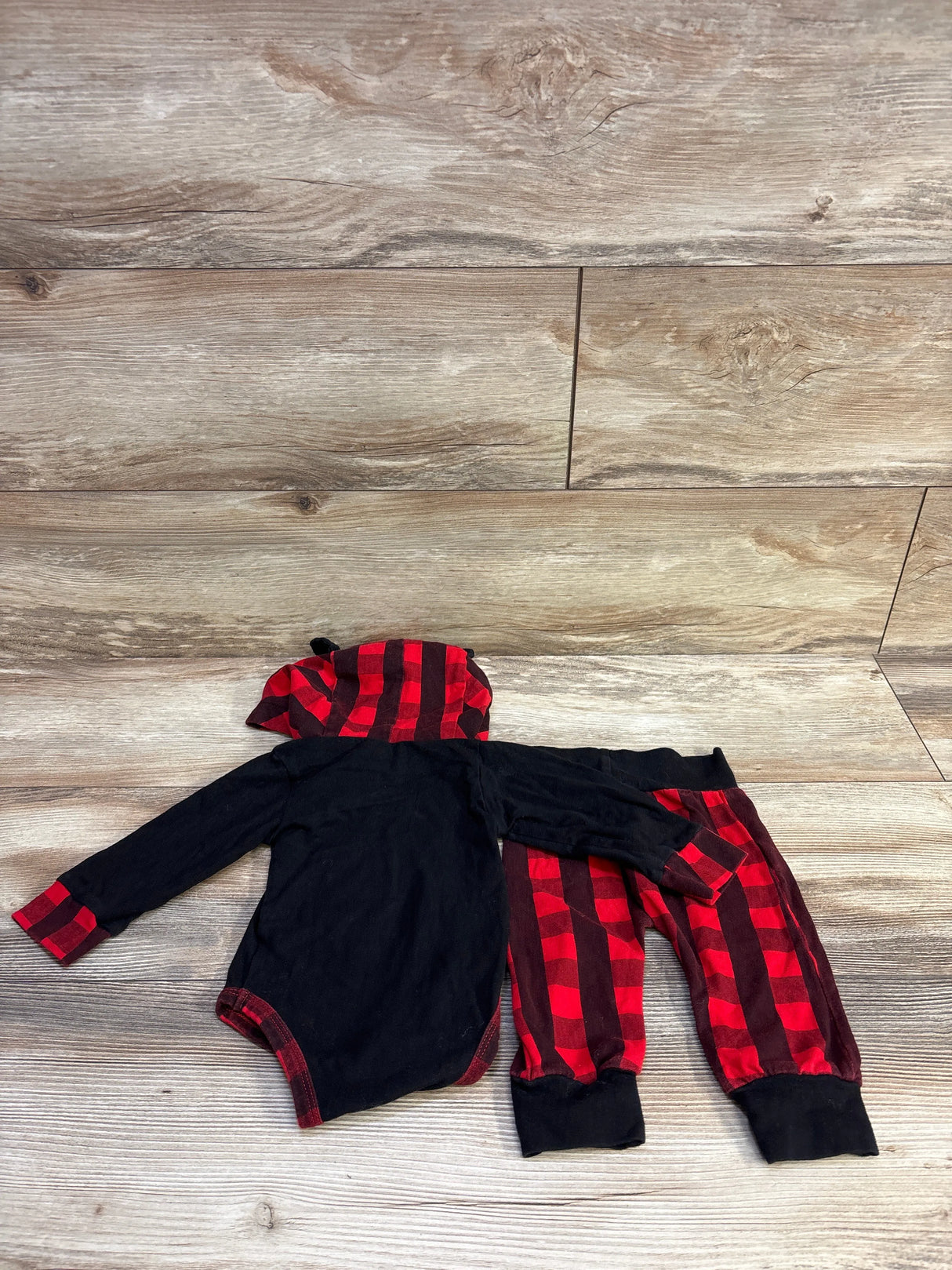Flat-lay of 3-6M baby bear hooded bodysuit and pants set showing black bodysuit with red plaid hood and pants on wood