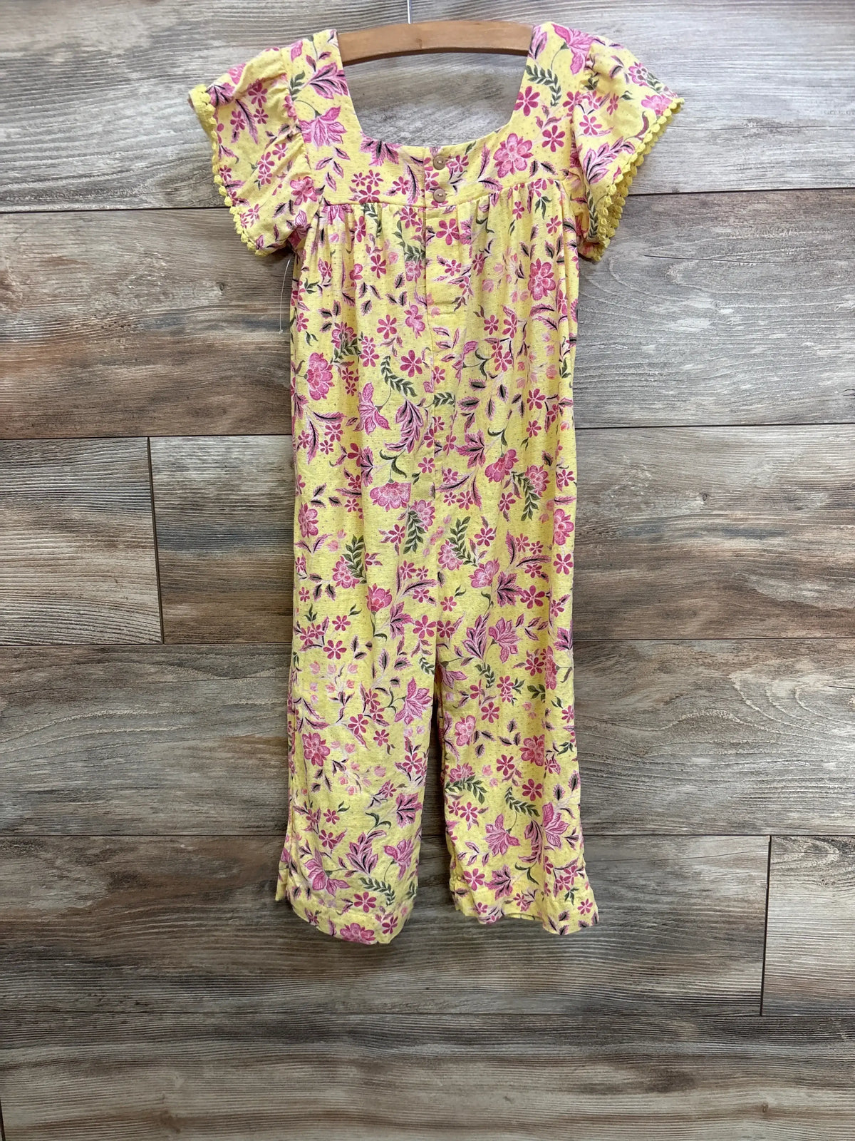 Front view of toddler yellow floral linen blend jumpsuit on wooden hanger showing puff sleeves, buttoned chest, and wide legs
