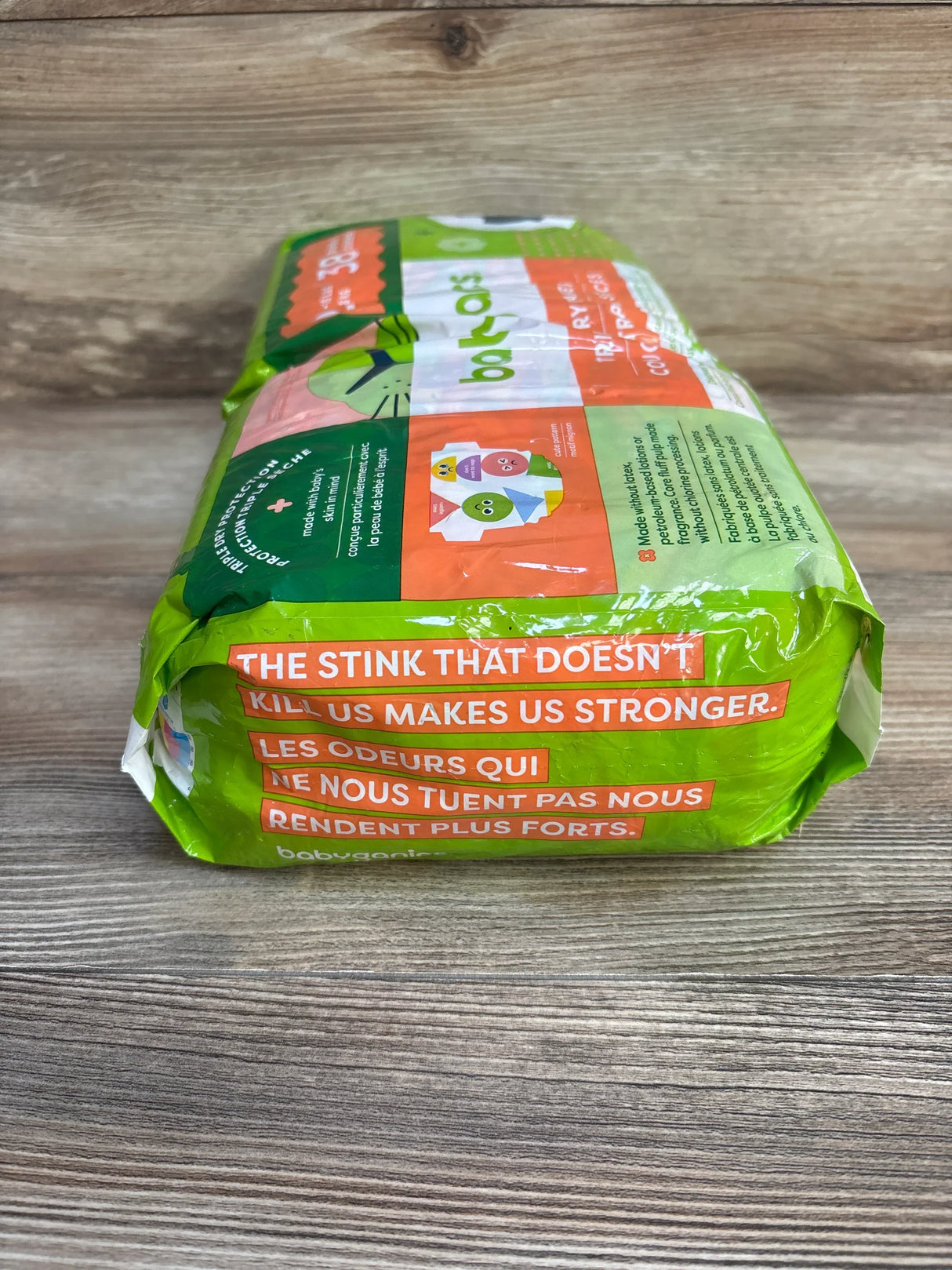 Low front view of Babyganics size 2 diapers showing headline 'The stink that doesn't kill us' and bilingual text on wood surface