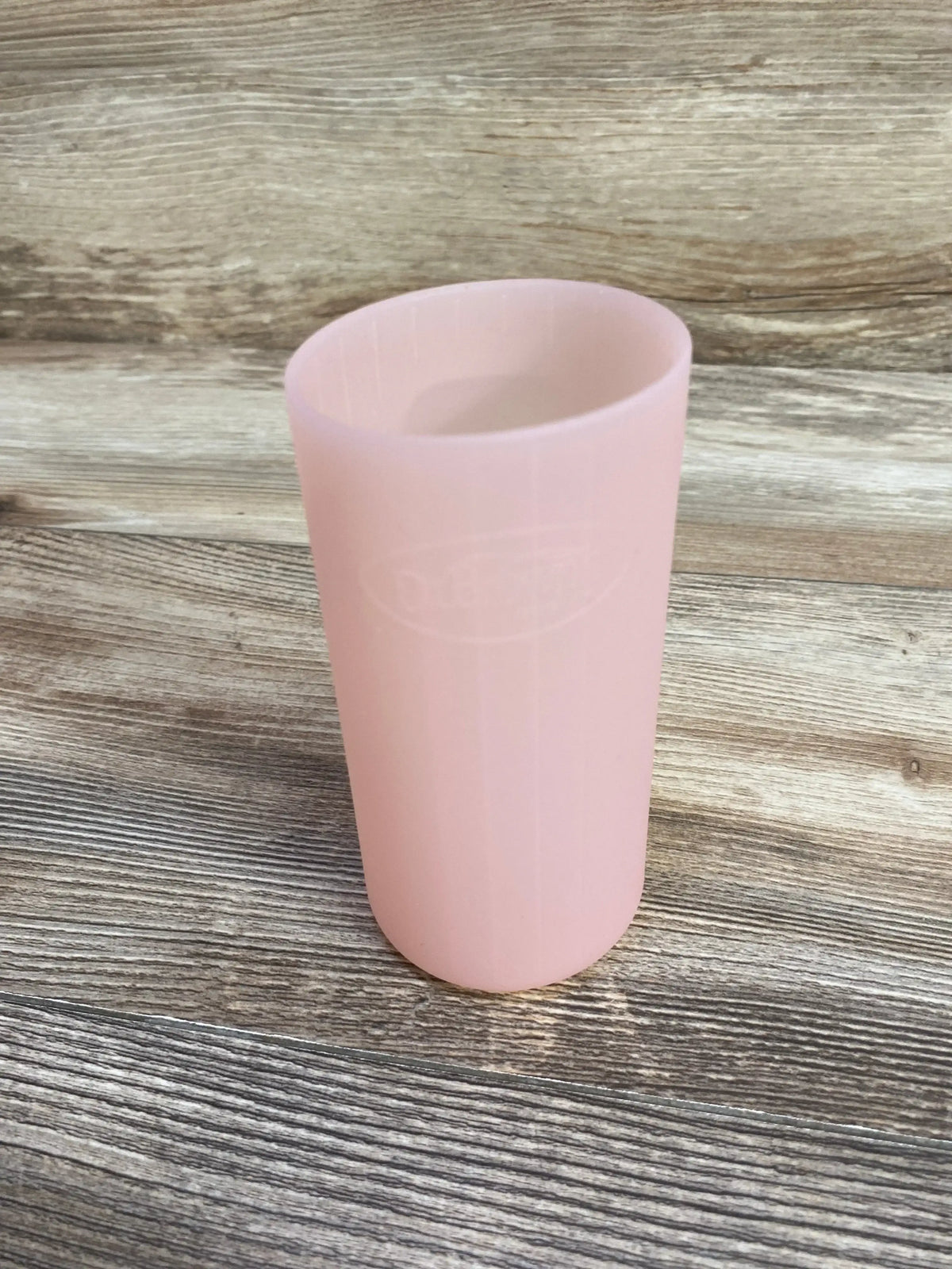 Angled top view of Dr. Brown’s narrow silicone 8 oz bottle sleeve showing pale pink ribbed texture on wood background