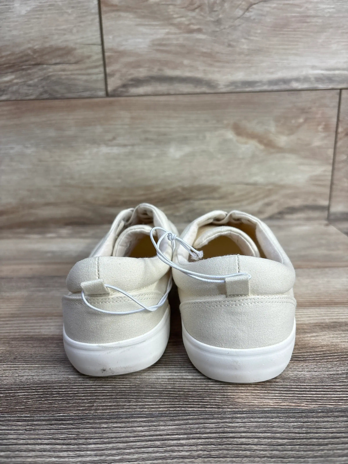 Back view of new Cat and Jack cream canvas casual sneakers with white rubber sole and security tag on wood plank floor