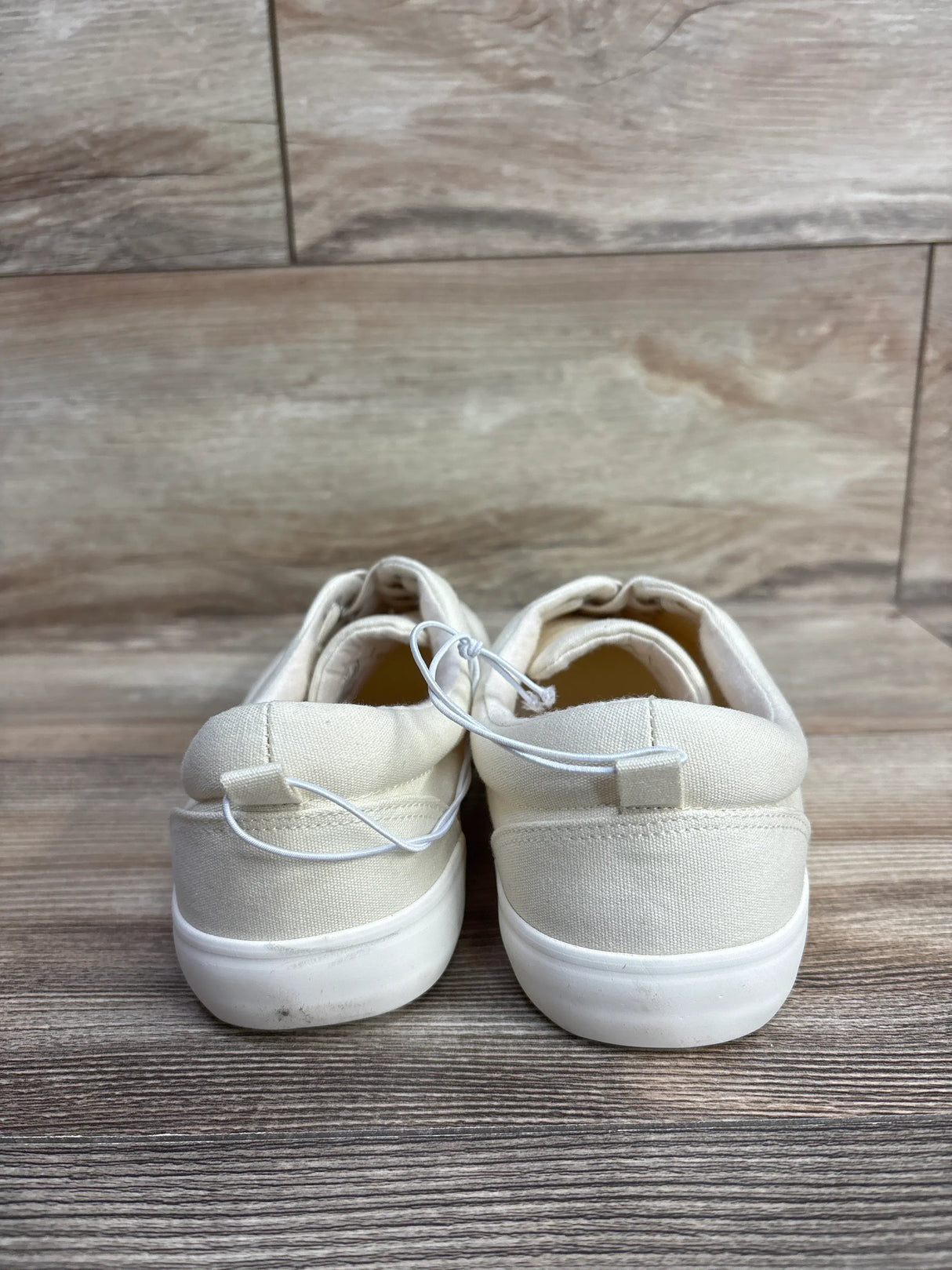 Back view of new Cat and Jack cream canvas casual sneakers with white rubber sole and security tag on wood plank floor