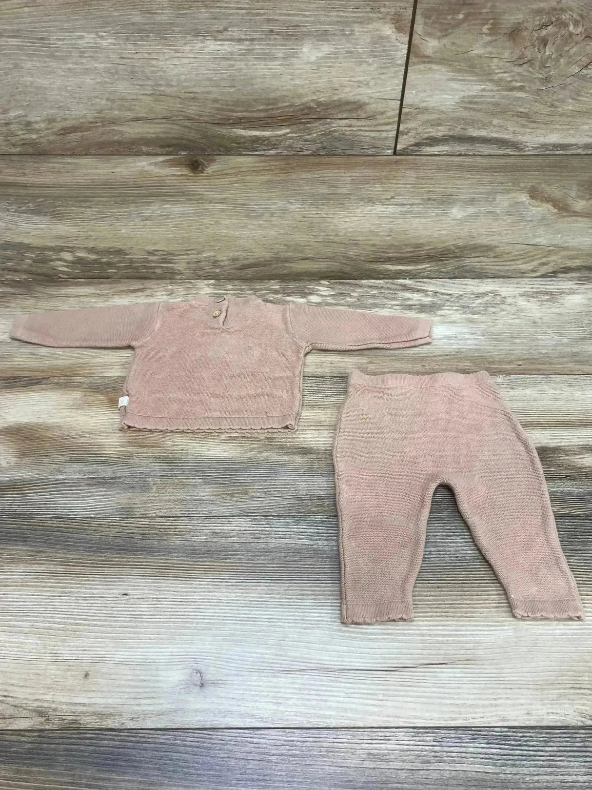 Flat lay of baby brown knit sweater and pants set (0-3m) showcasing two-button neckline and scalloped hem on wood background