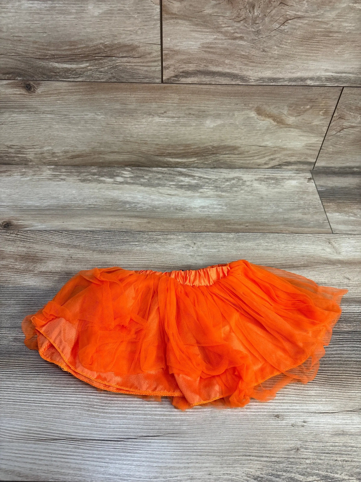 Top view of the orange Bow Tutu showcasing layered tulle and an elastic waistband on a wood-look floor