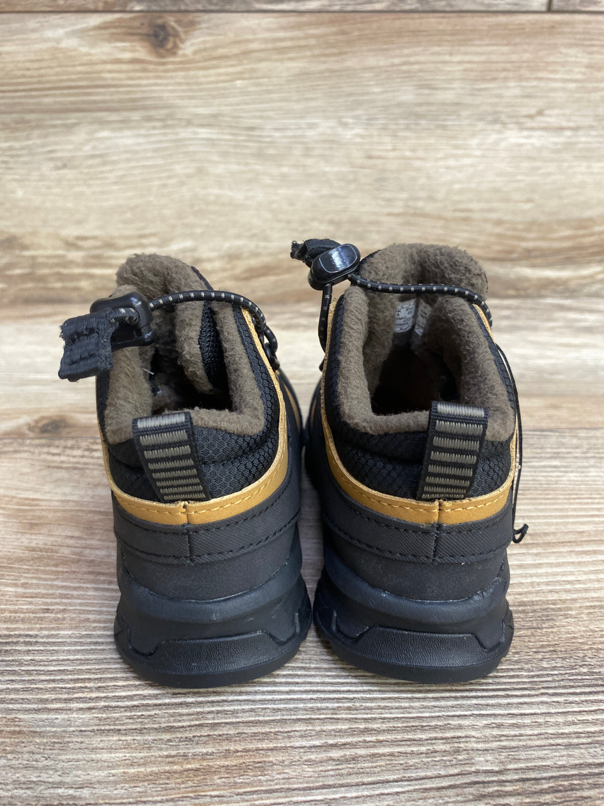 Back view of black and brown toddler winter boots with fleece lining on wooden floor