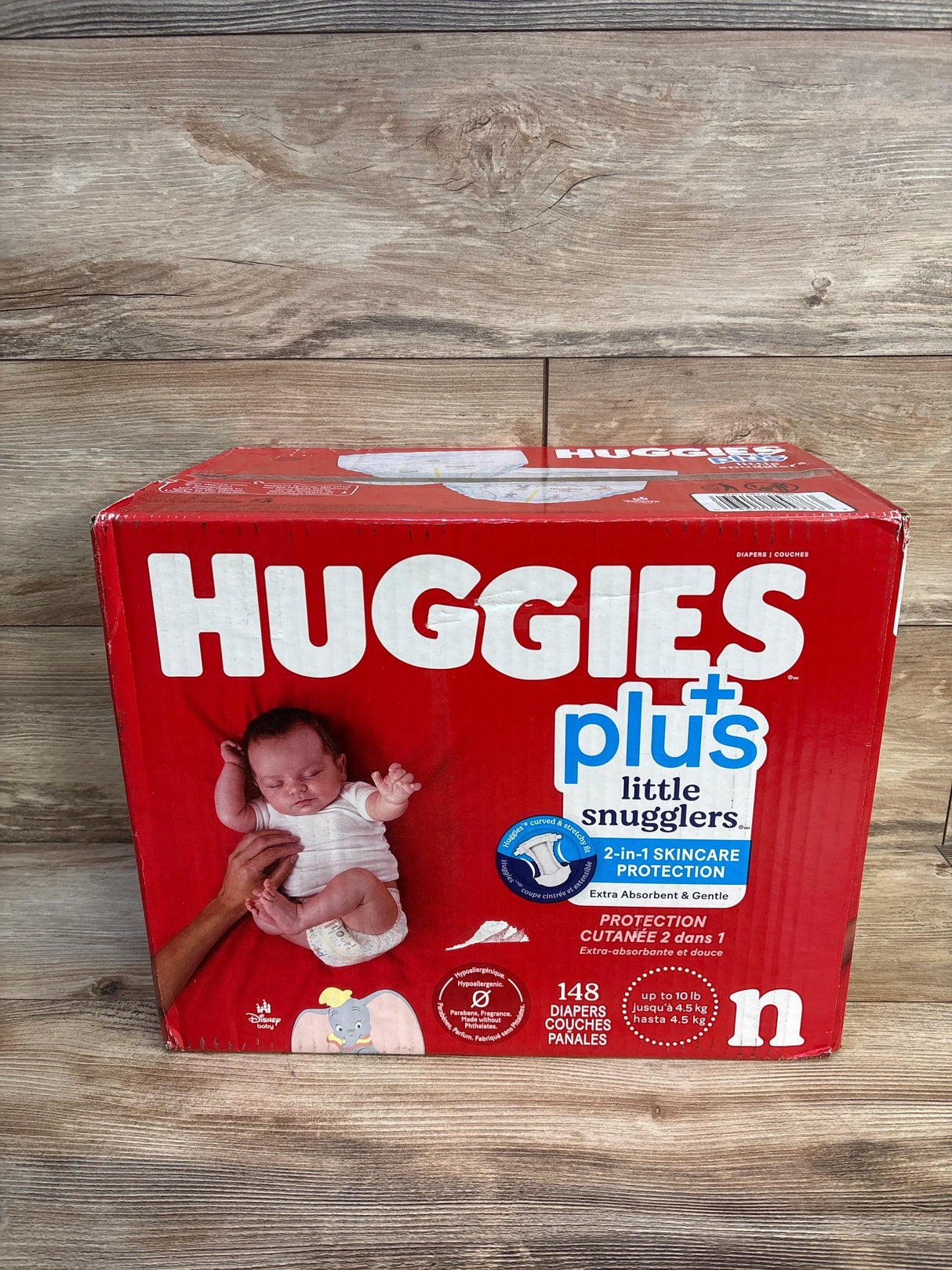 Front view of Huggies Little Snugglers Plus newborn diaper box showing 148-count pack and baby image on wood floor