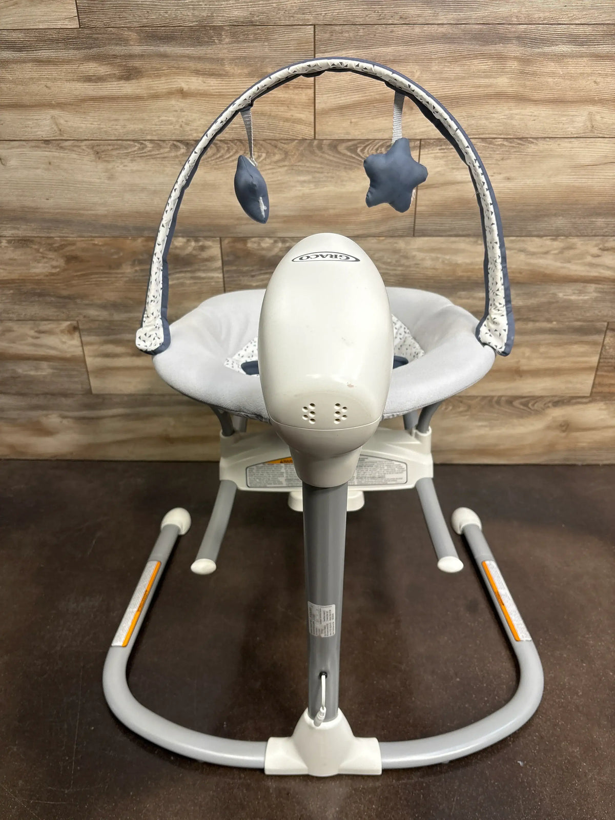 Front view of Graco Soothe ‘n Sway LX Swing with Portable Rocker in Derby showcasing two soft toys and a padded seat on wood flooring