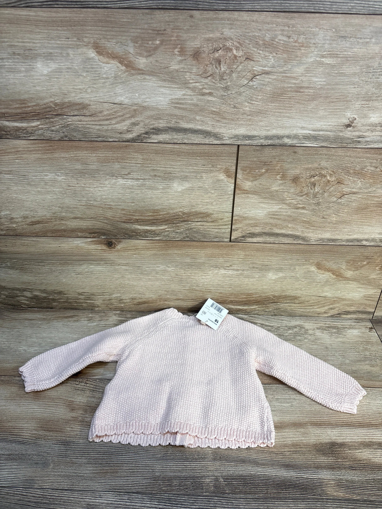 Light pink knit baby sweater with tag displayed on wooden background