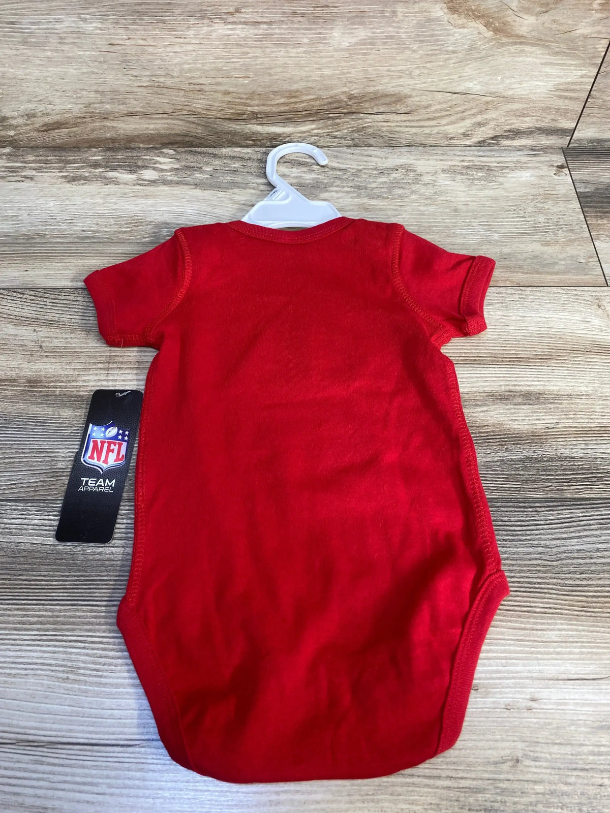 Red short sleeve baby bodysuit with NFL Team Apparel tag on wood background
