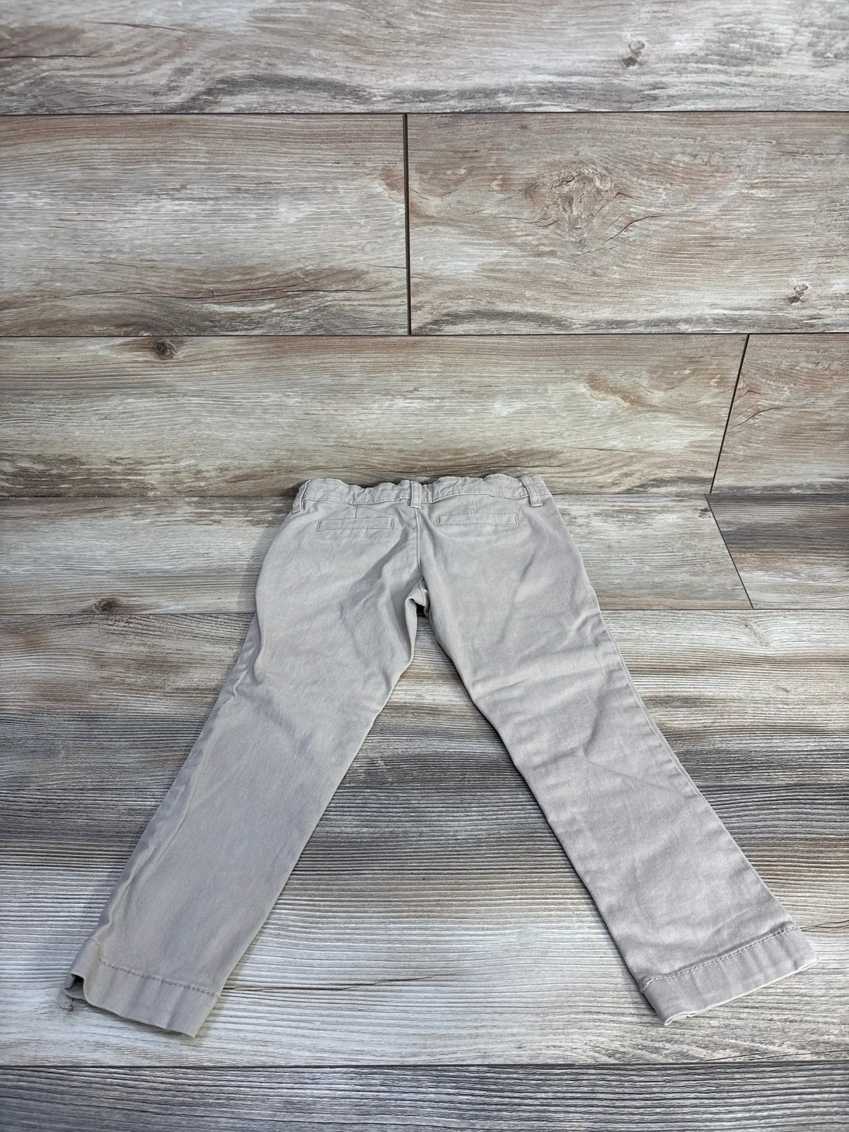 Flat lay back view of khaki toddler skinny stretch pants showing elastic waistband and back welt pockets on wood floor
