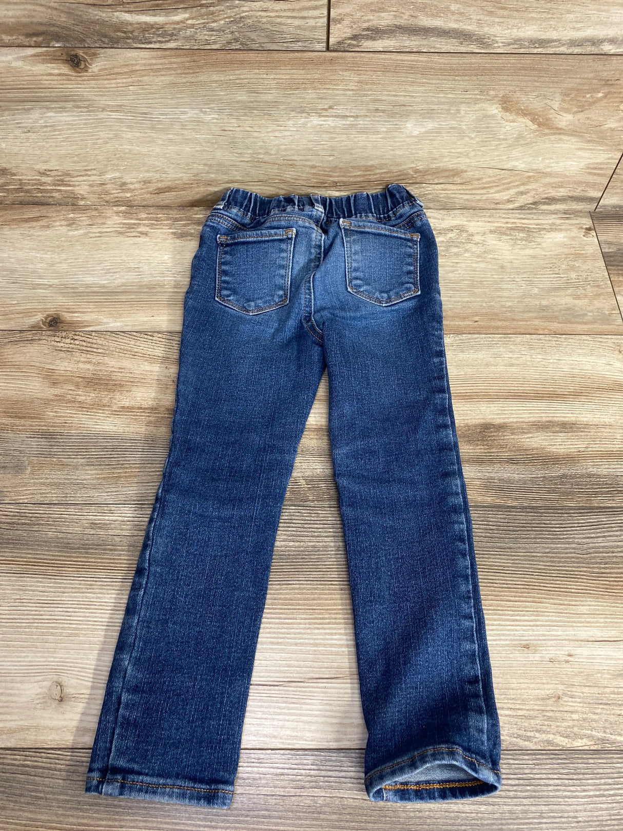 Children's dark blue denim jeans with elastic waistband, back view on wood floor