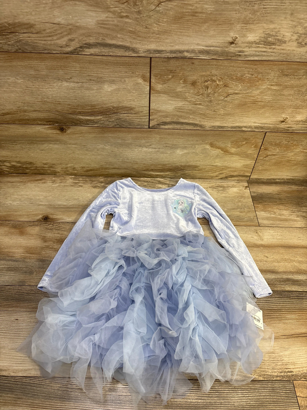 Flat lay of blue Disney Frozen long-sleeve ballerina tulle dress showcasing ruffled tulle skirt and Elsa chest patch on wood floor background