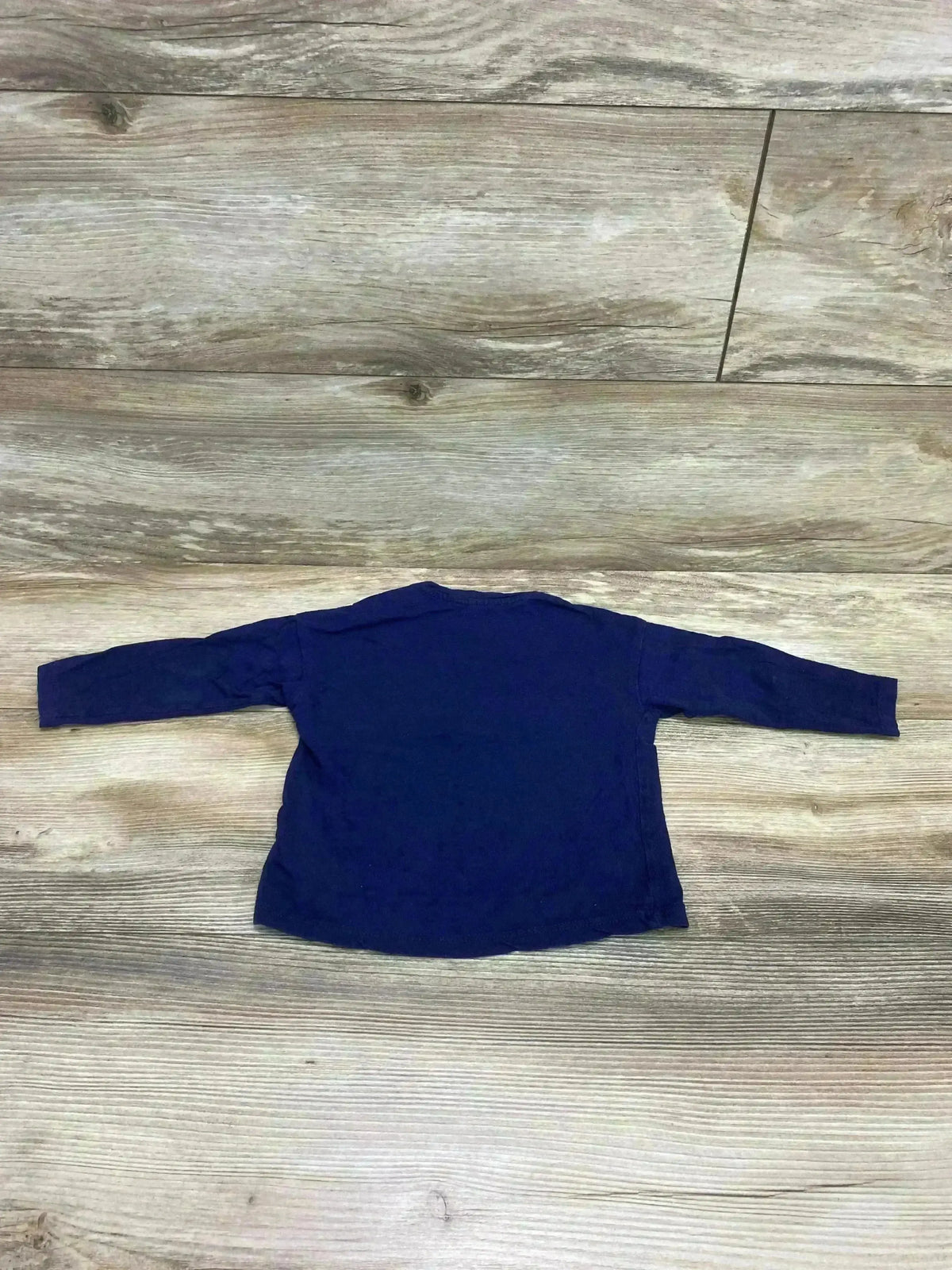 Back view of H&M navy blue long-sleeve baby shirt (9-12 months) showing plain back and long sleeves on wood plank background