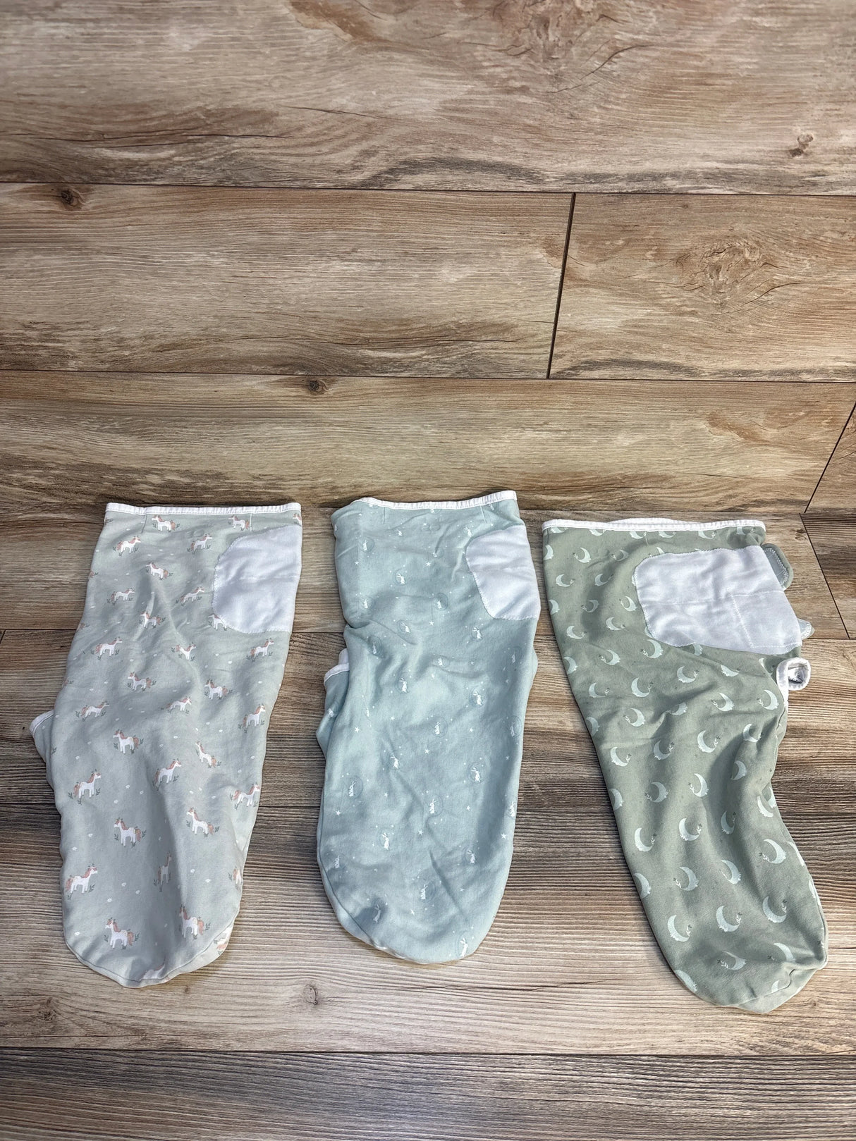 Three pastel baby sleep sacks with animal and moon patterns on wood floor