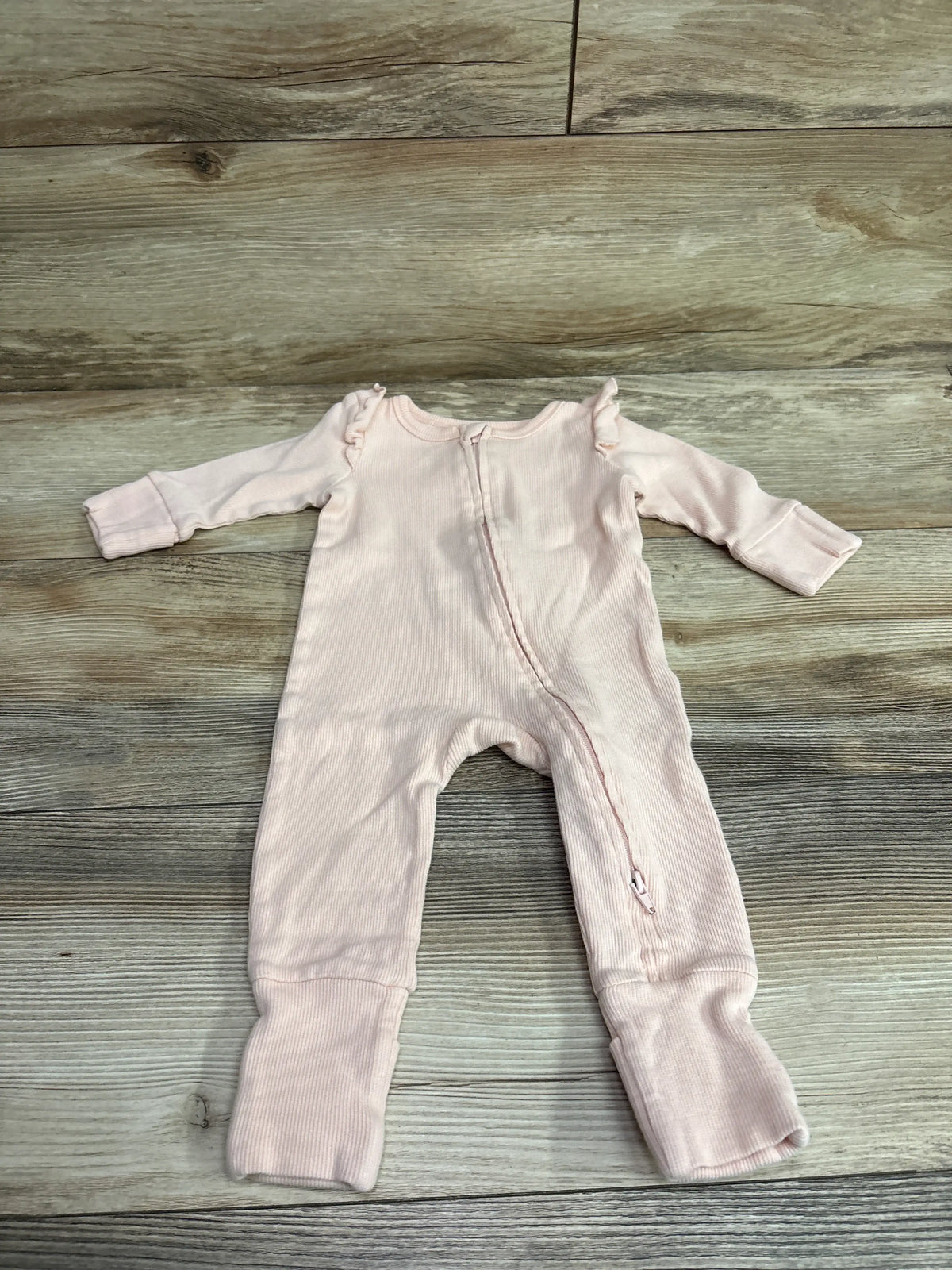 Front view of pink Cotton On Baby organic ribbed sleeper, size 3 to 6 months, with ruffled shoulders and zipper on wood grain