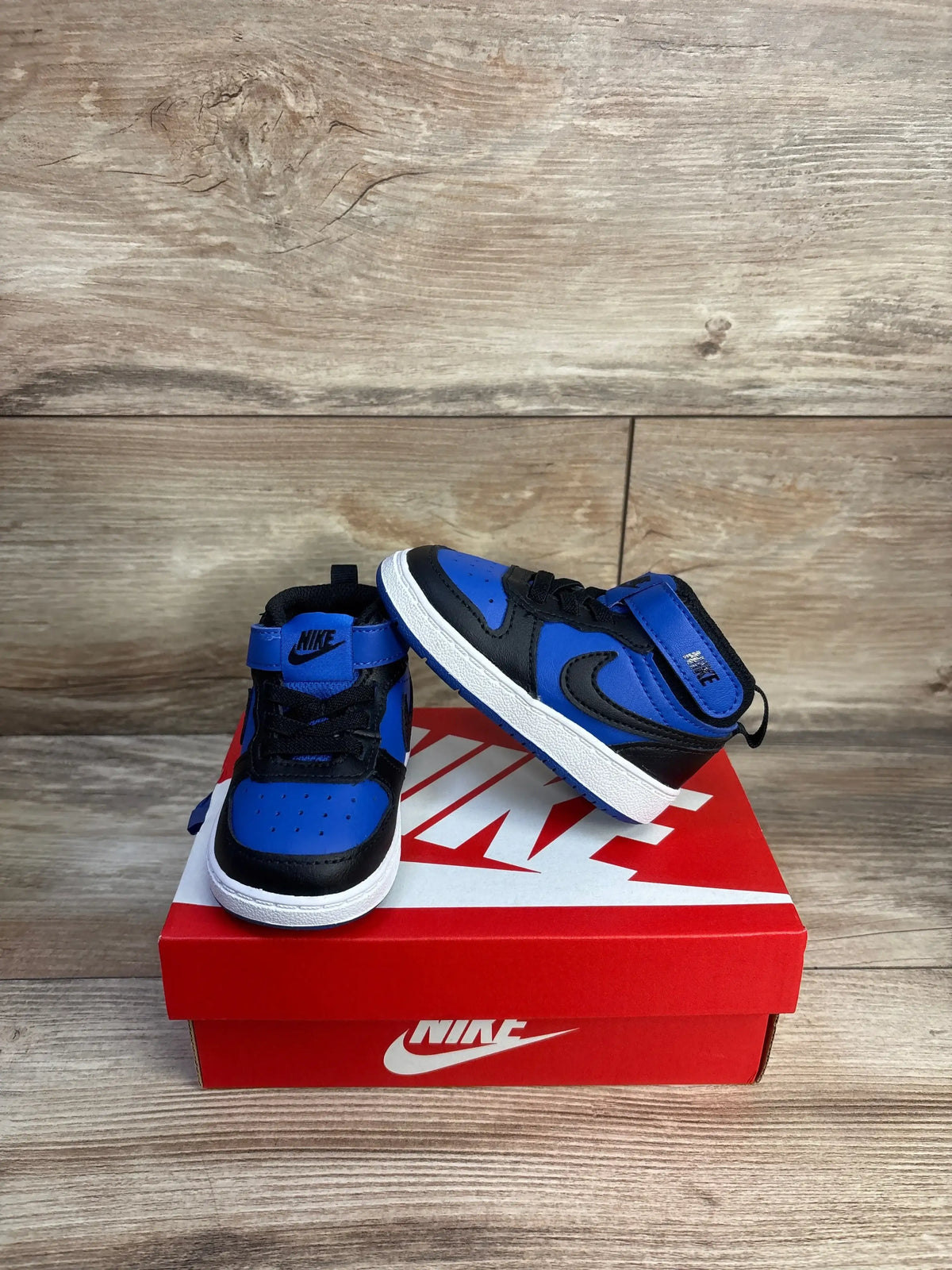 Front three-quarter view of Nike Court Borough Mid 2 toddler sneaker in black and game royal showing Velcro strap on a red Nike box