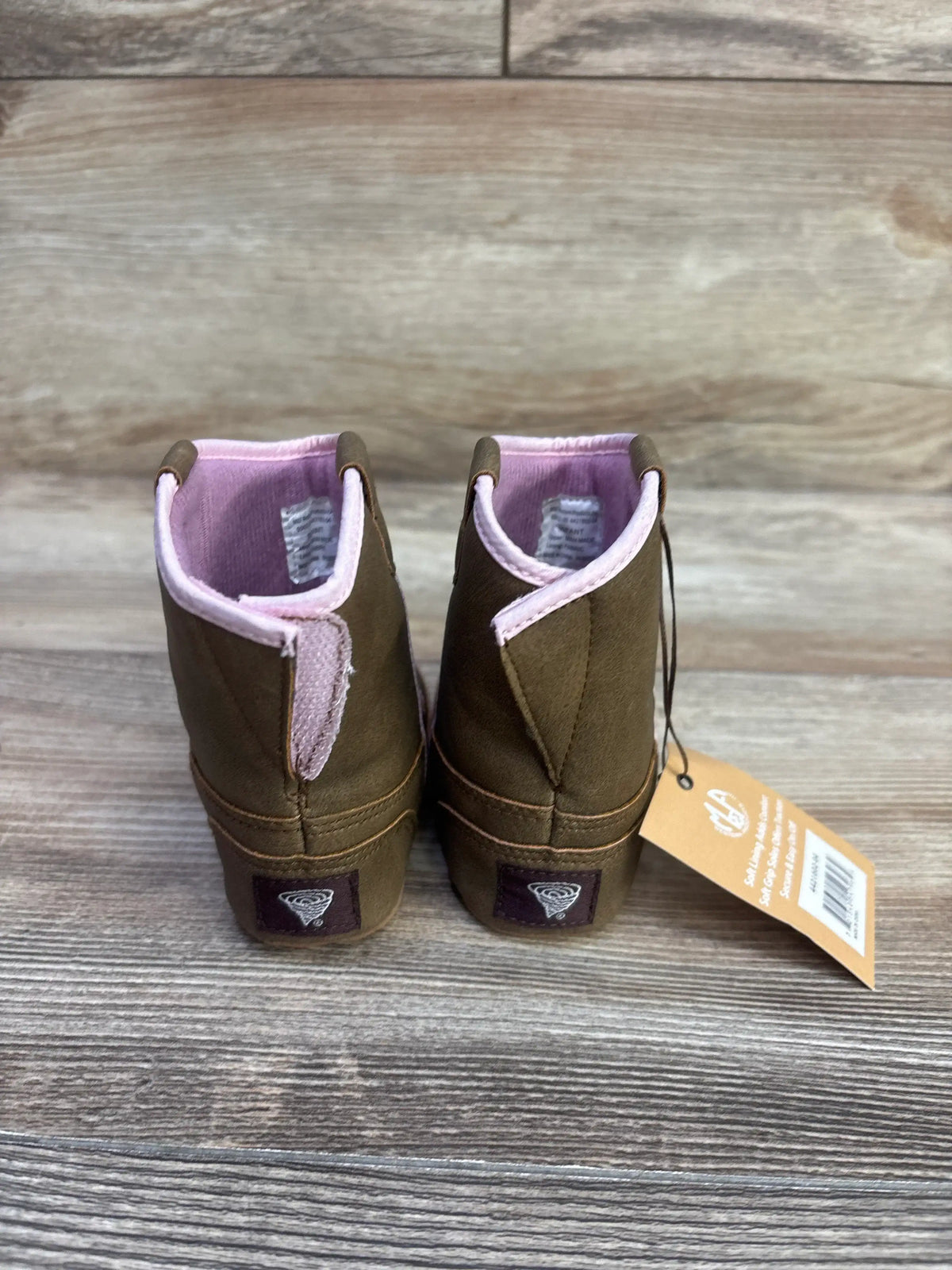 Rear view of Twister Gracie baby buckers boots showing pink interior lining, heel logo, and attached tag on wooden background