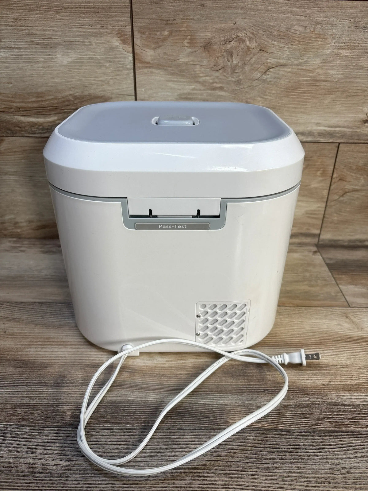 Front view of UV Care Multipurpose Sterilizer Lite 1 showing hinged lid, front vent and coiled power cord on wood floor background