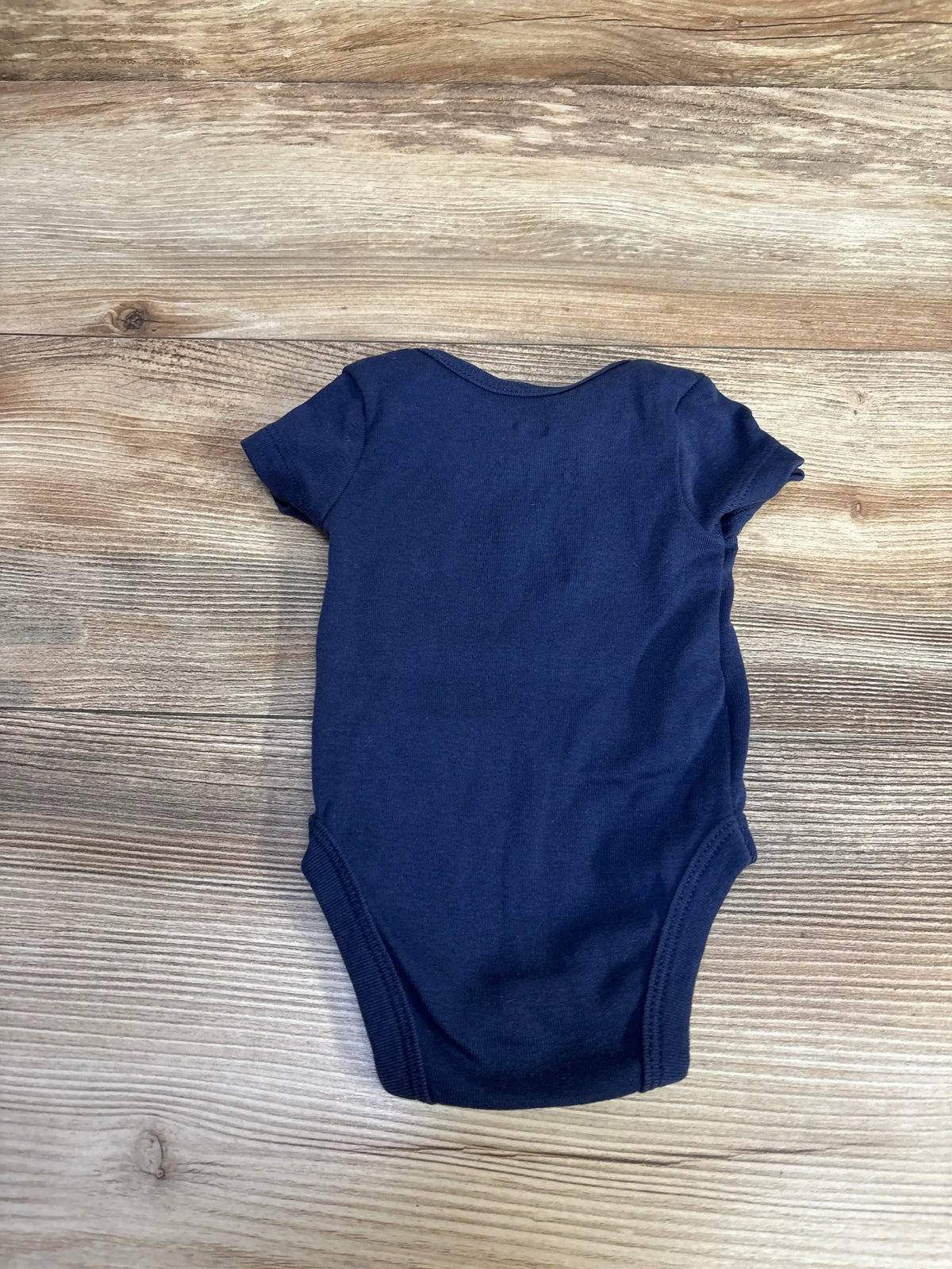Top view of Nike navy blue 3 month baby bodysuit showing back and short sleeves on wood background