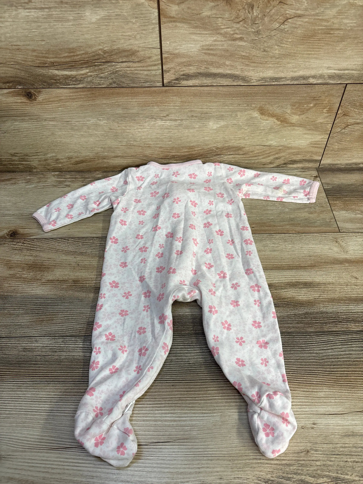 Top view of Little Me white floral sleeper showcasing pink flower pattern and footed legs on a wood floor