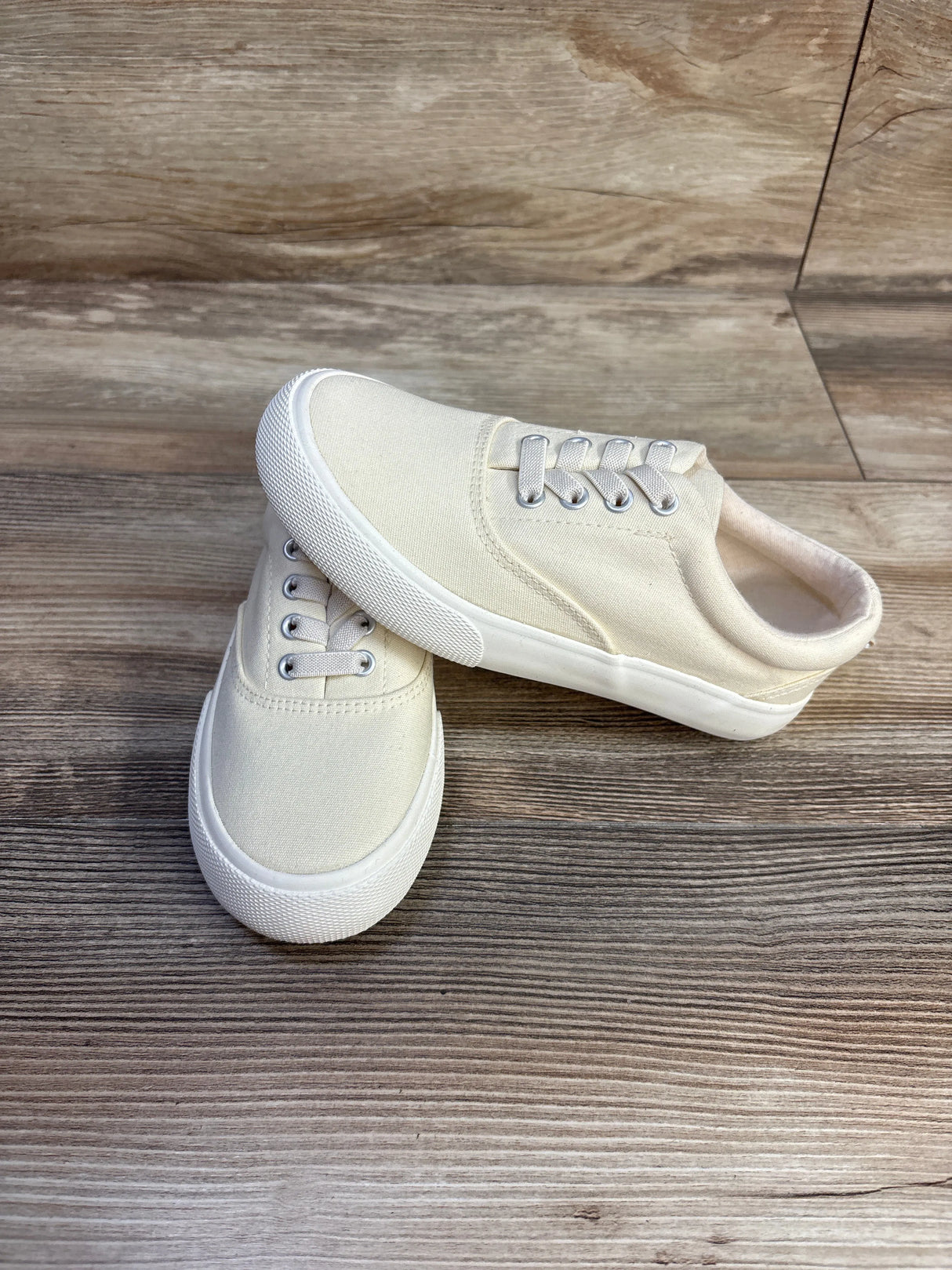 Angled view of Cat & Jack Tyler off-white toddler slip-on sneakers, canvas upper, elastic laces, white sole on wood floor