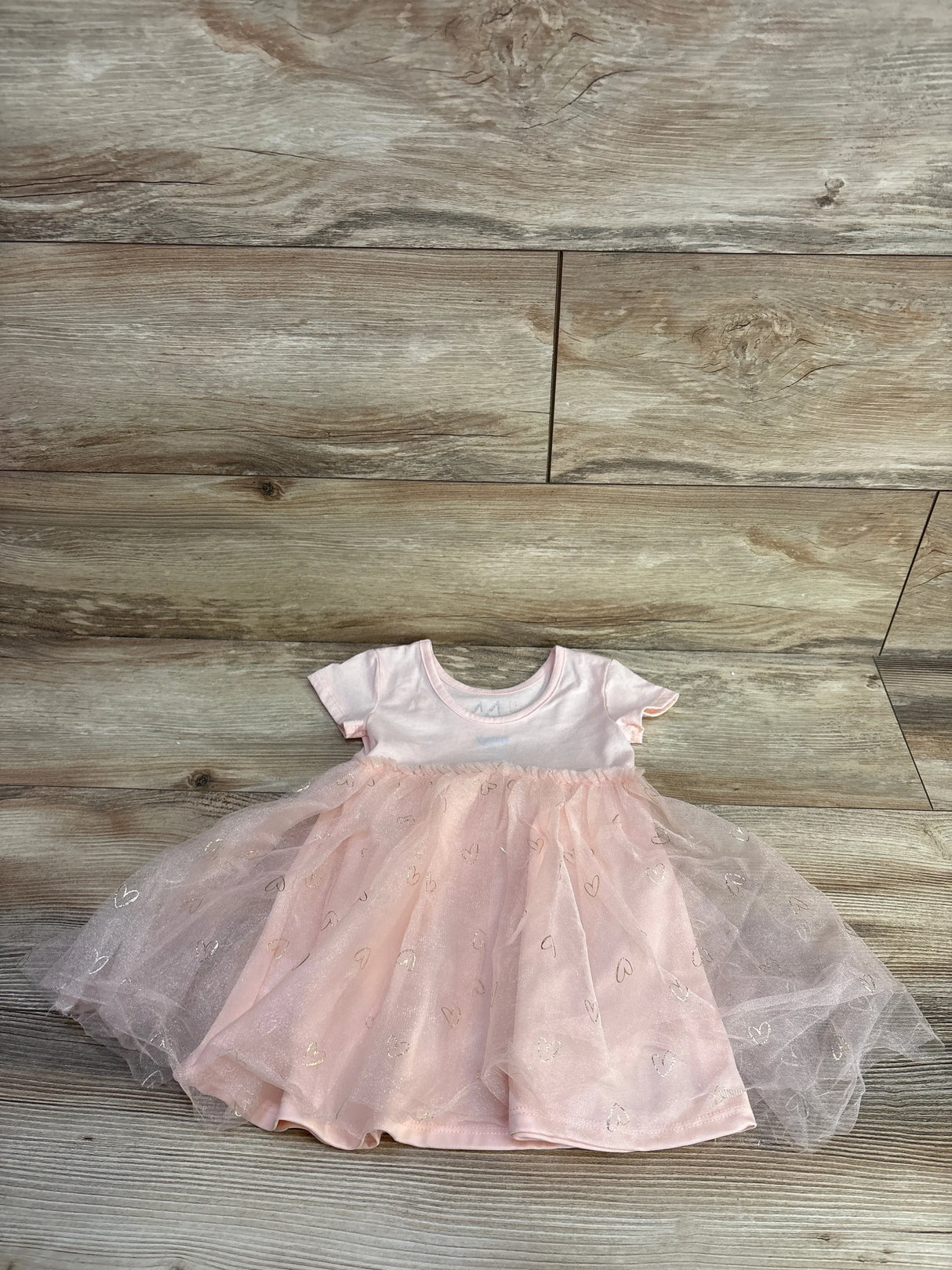 Flat lay of pink tulle baby dress showcasing glitter heart tulle skirt and short-sleeve bodice on wood floor