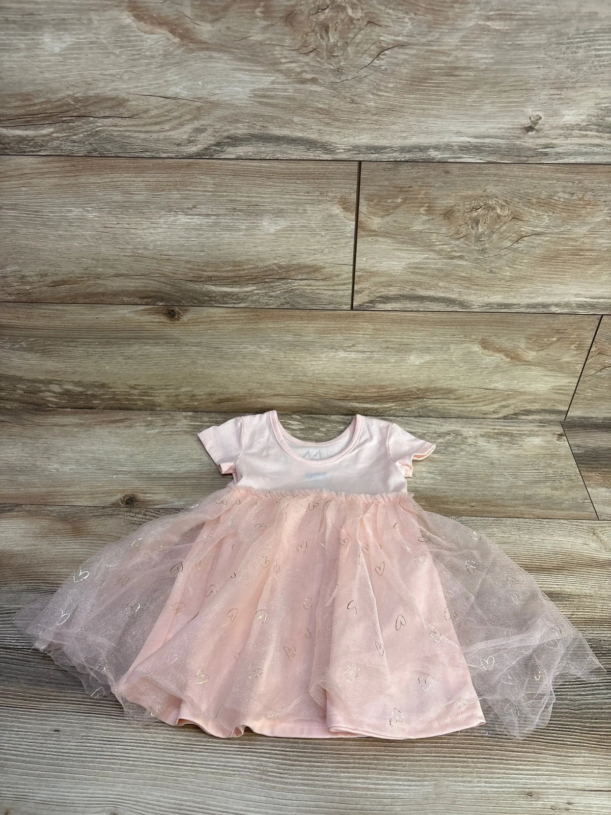 Flat lay of pink tulle baby dress showcasing glitter heart tulle skirt and short-sleeve bodice on wood floor