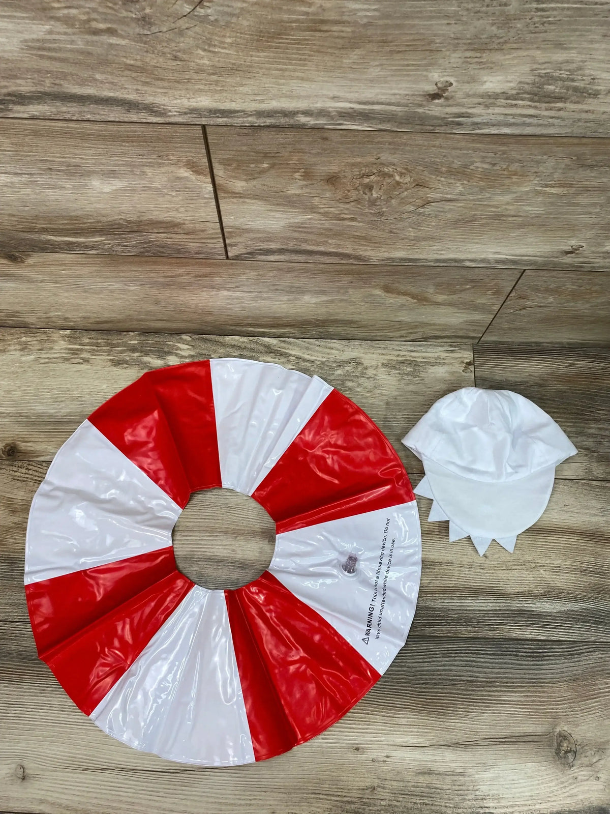 Top view of Pinkfong Baby Shark costume showing a red-and-white inflatable ring and shark-fin cap on wood flooring