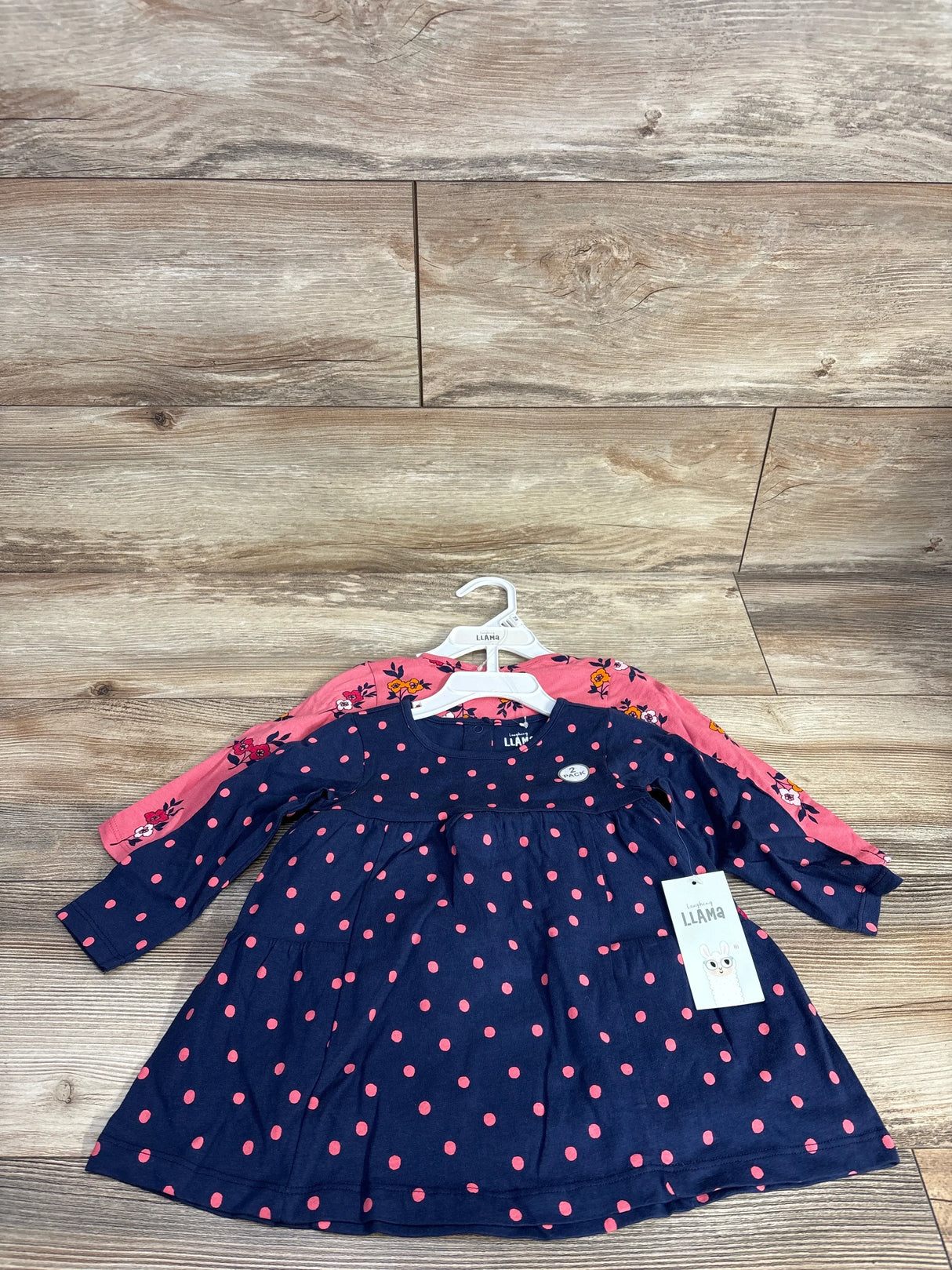 Front view of girls 2pc dress set with navy polka dot dress over pink floral dress on hangers on wood floor