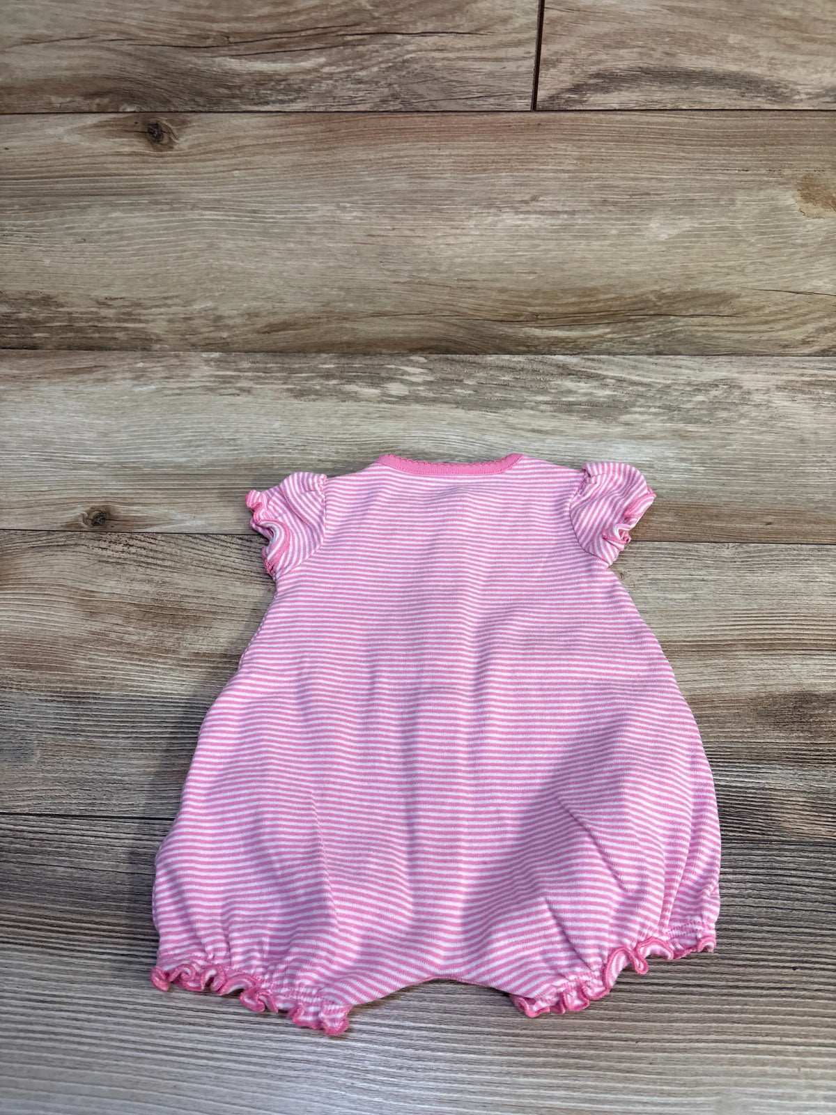 Back view of Simple Joys shortie romper in pink and white stripes showing ruffled cap sleeves and elastic ruffled leg openings on a light wood background