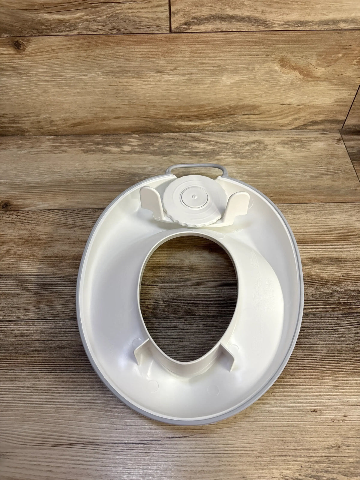 Top view of Baby Bjorn Toilet Trainer Seat showcasing its handle and splashguard with a wood-grain background