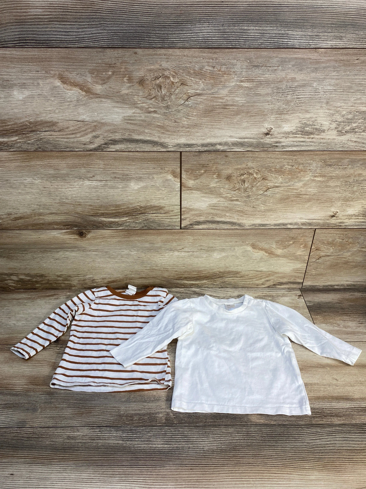 Two long sleeve kids shirts, one brown striped and one plain white, on wood background